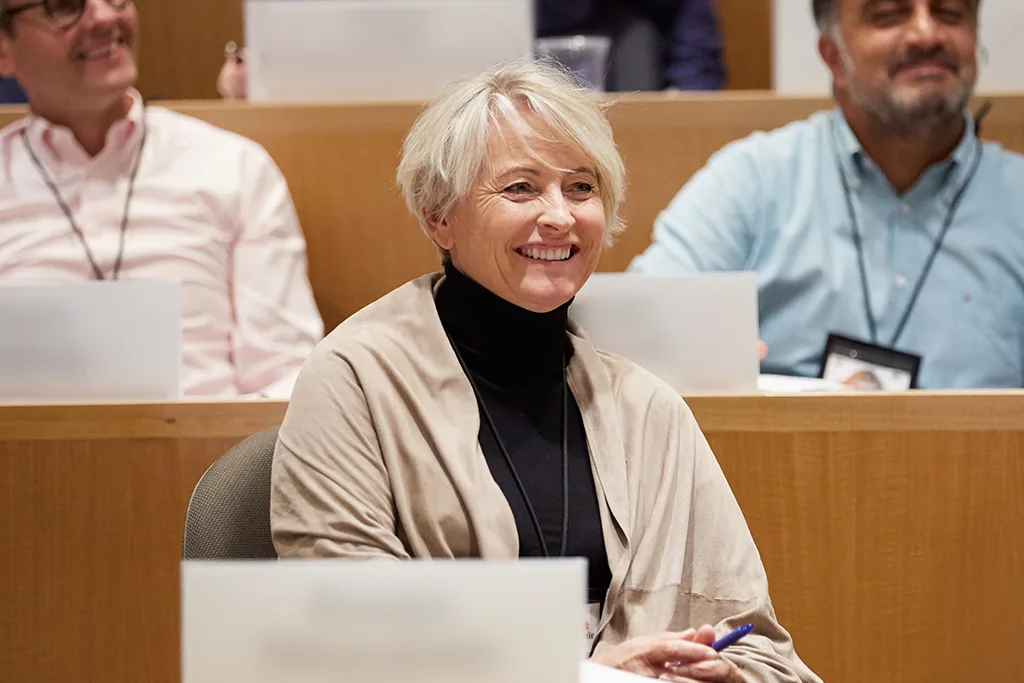 Participants sit while listening to a classroom lecture with the focus on the woman in front of two males seated behind her