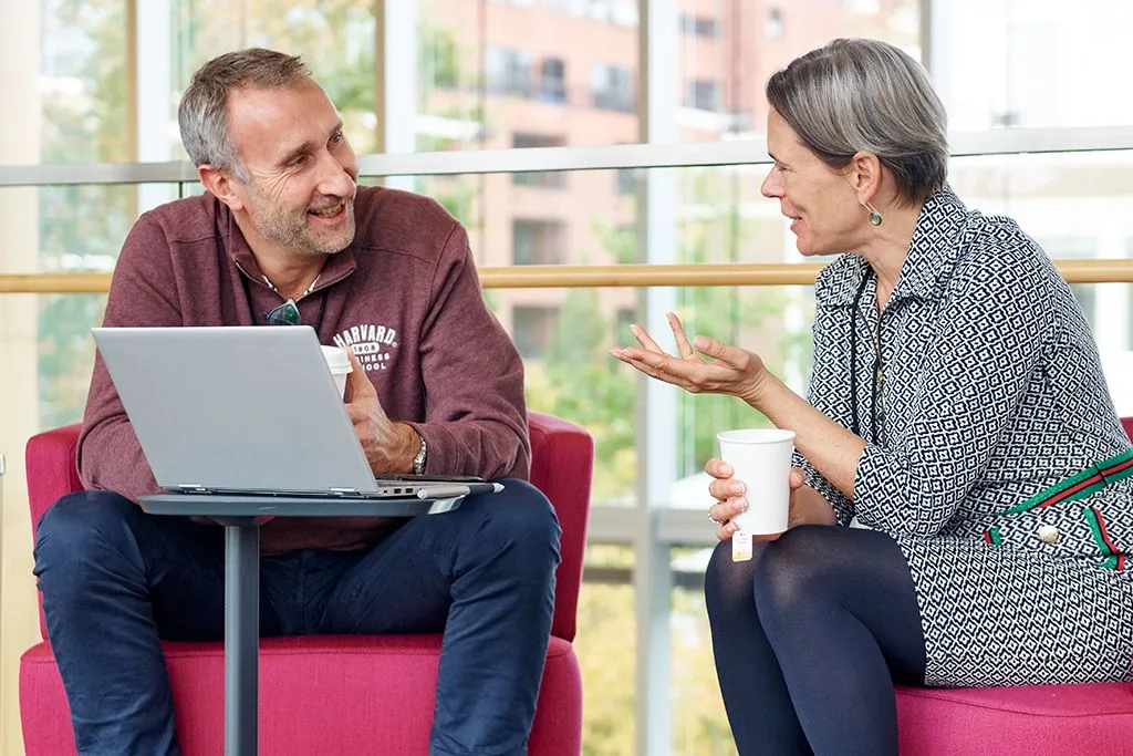 A male and a female executive talk sitting down with an open laptop
