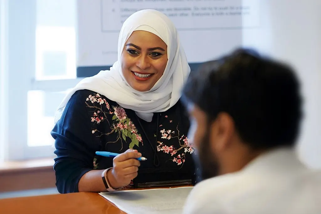 Female participant engaged in meeting room session discussion, listening on as she sits with a pen and paper taking down notes