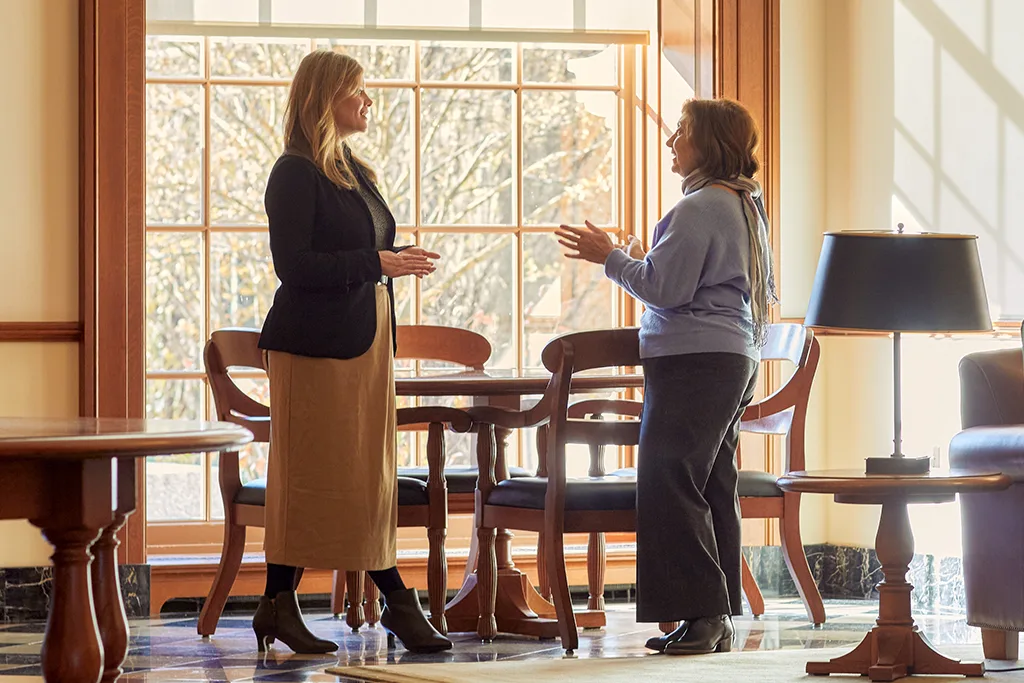 Two women talking in a sunlit room near a large window