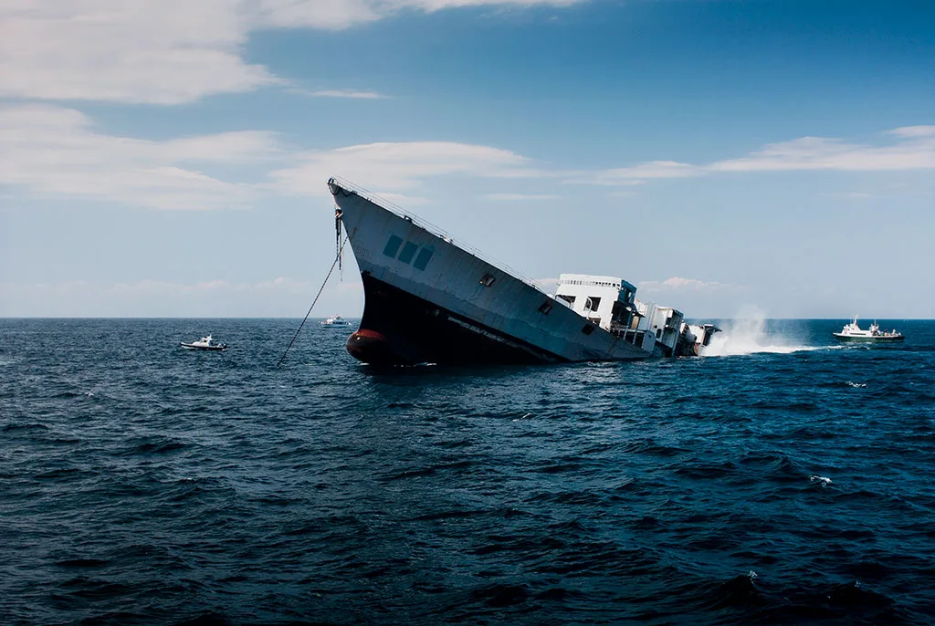 Large decommissioned Navy ship tilting as it sinks into the ocean to become an artificial reef.