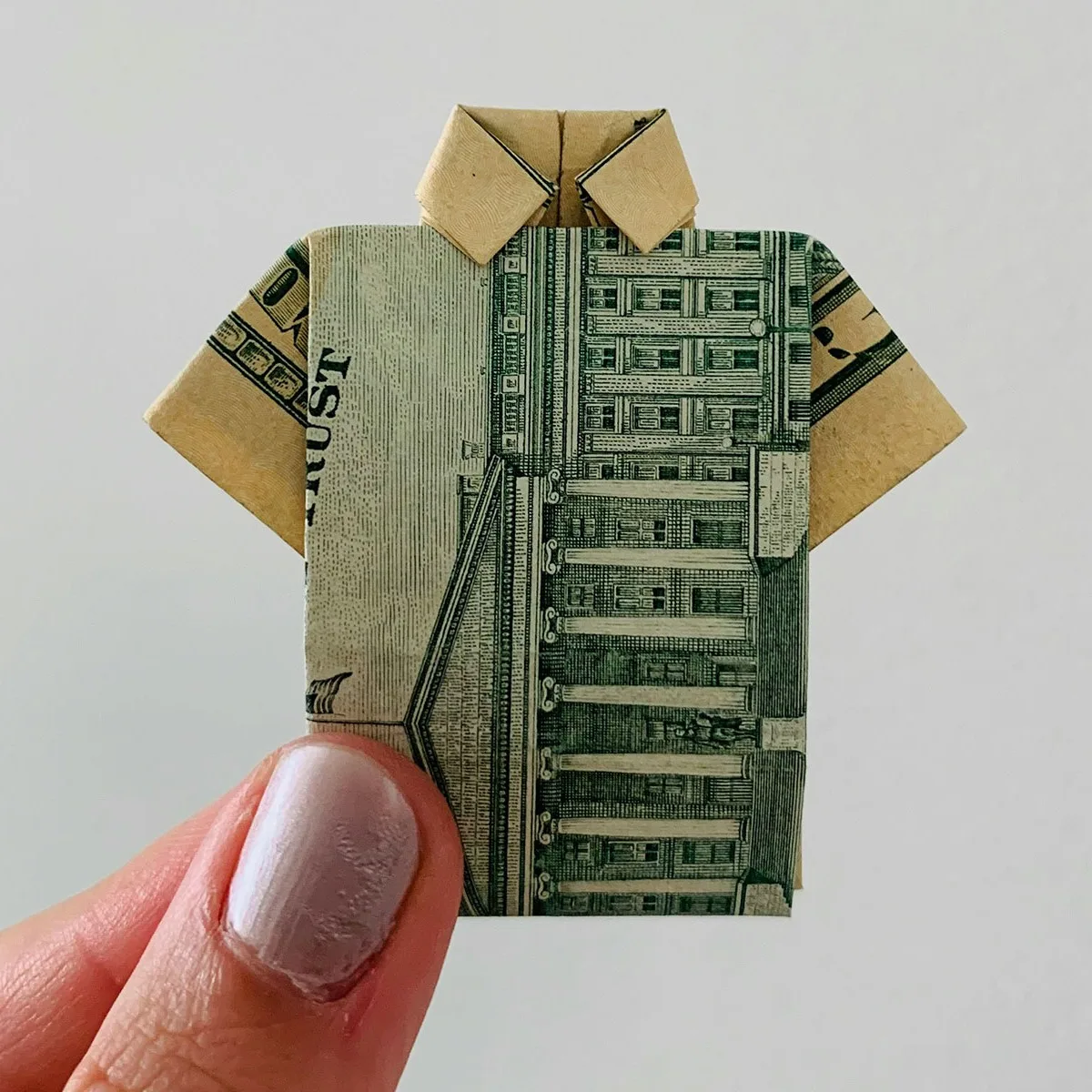 Hand holding a dollar bill folded into the shape of a shirt. 