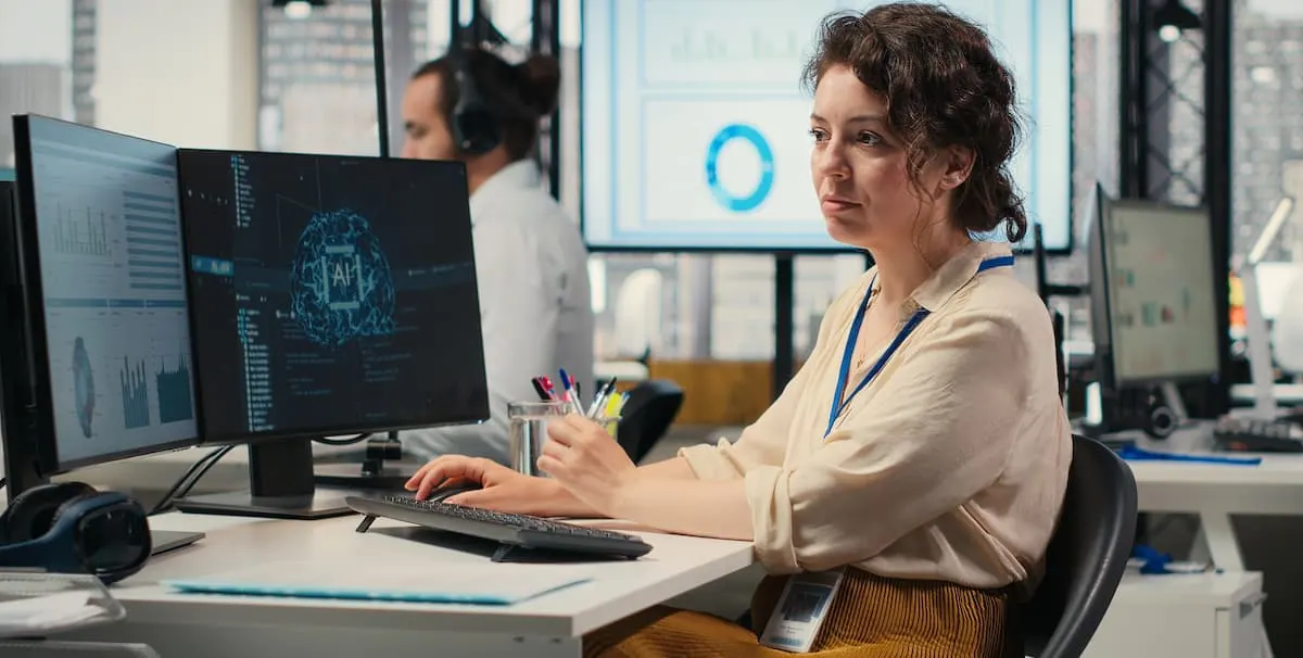 Professional working at a desk with multiple computer monitors displaying AI-generated insights, data visualizations, and analytics dashboards in a modern office setting.