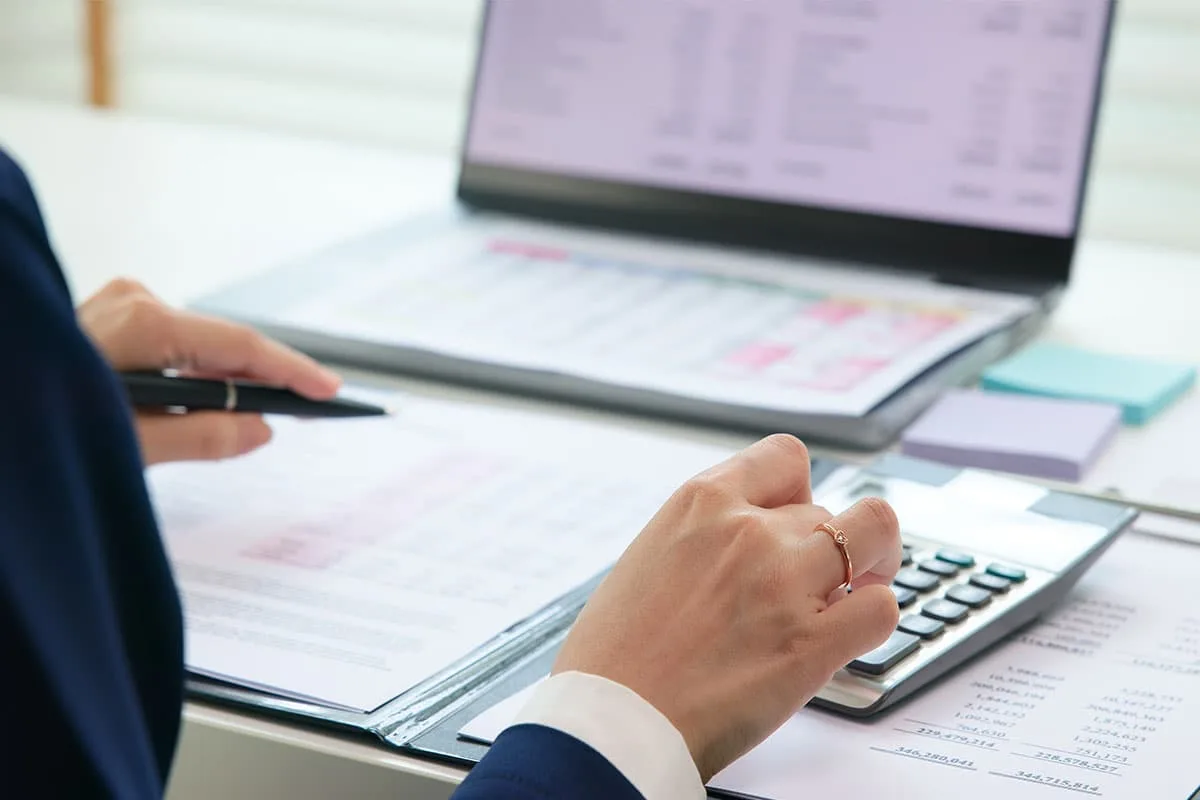 Person reviewing financial documents and using a calculator beside a laptop.