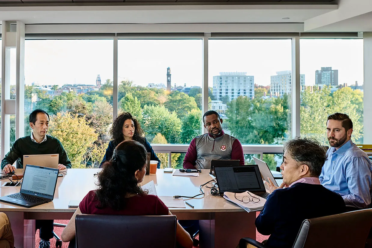 Executive participants gather to talk around a large round table in a conference room with large windows and natural light