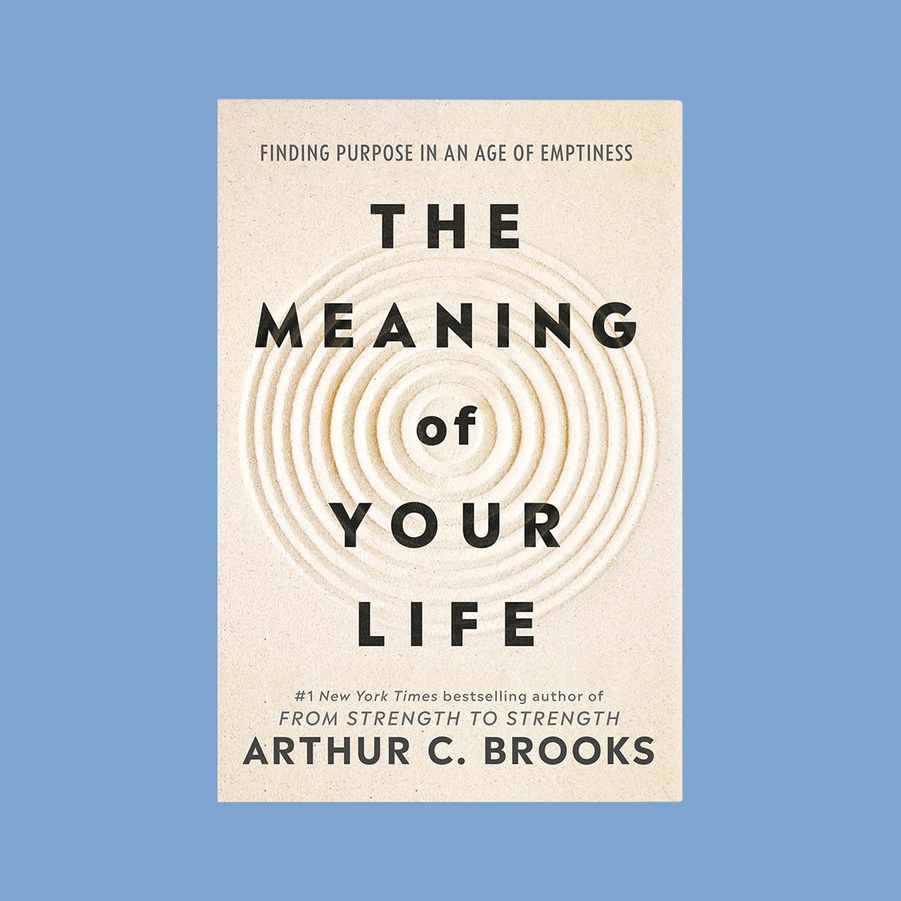 Book cover on blue background. Cover has concentric circles in sand, top text reads "Finding purpose in an age of emptiness," in middle "The Meaning of Your Life," below "#1 New York Times bestselling author of From Strength to Strength Arthur C. Brooks."