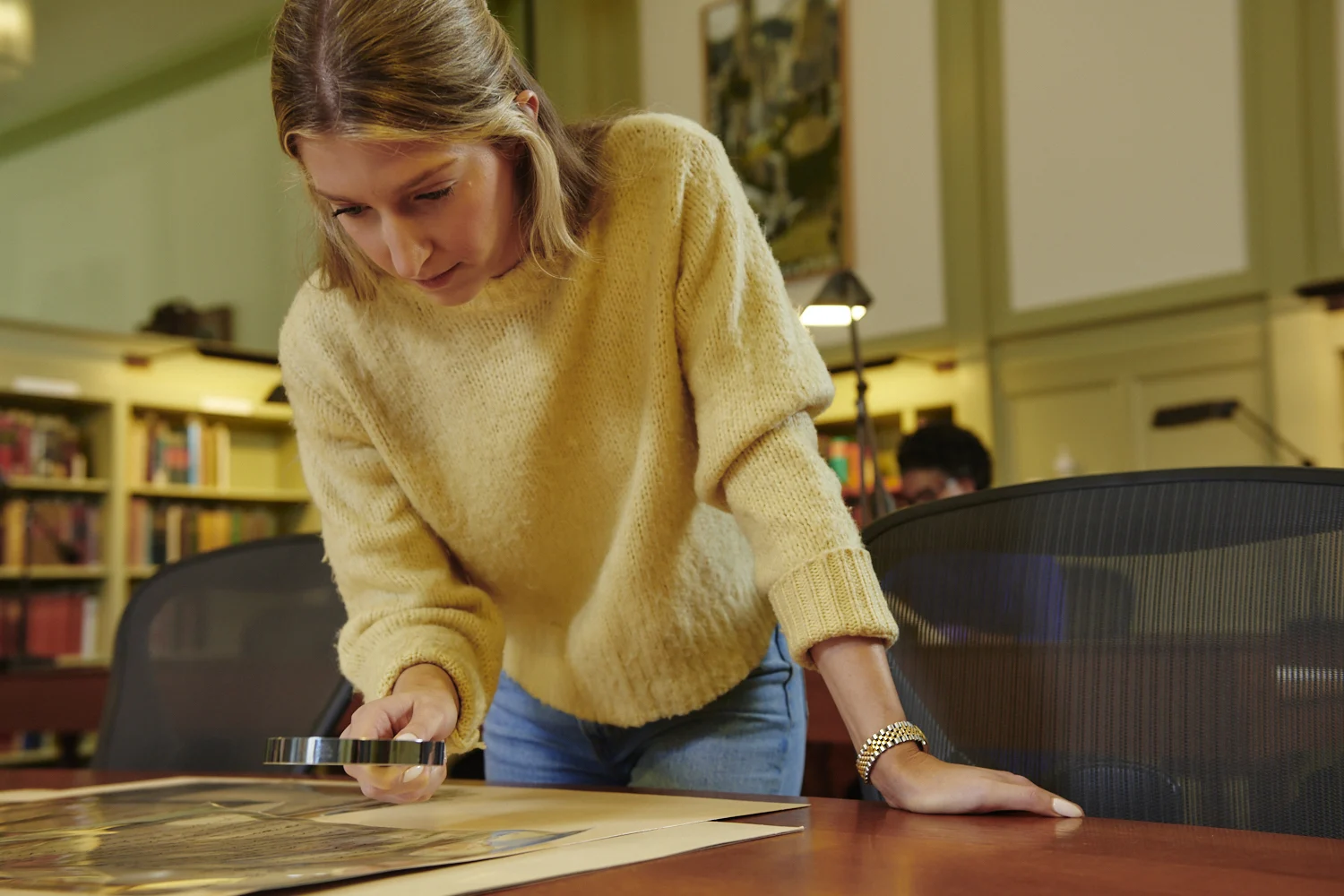 Woman leaning over table inspecting document with magnifying glass