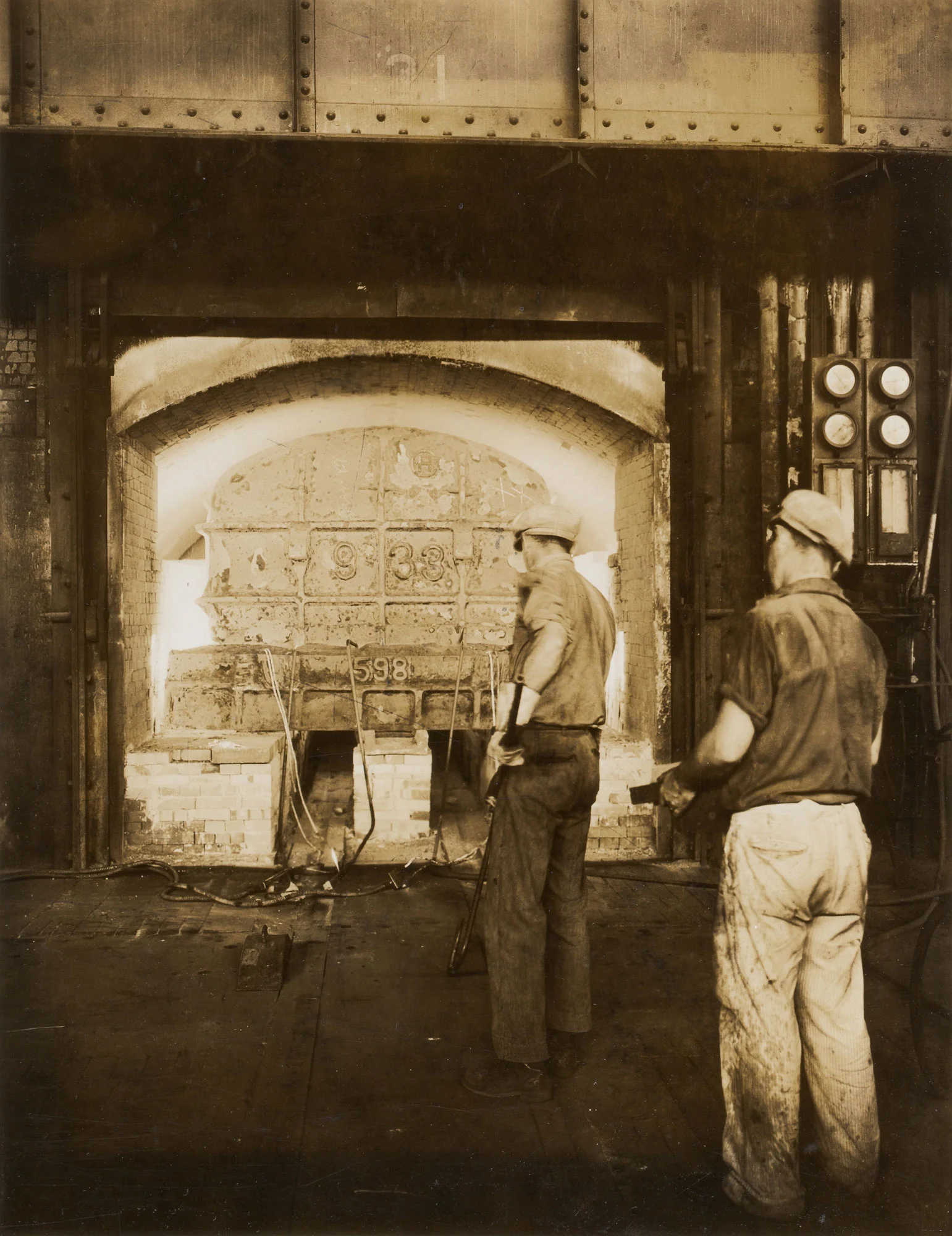 Two workers stand before heat treating furnace used for annealing steel sheets at Gary Steel Works.