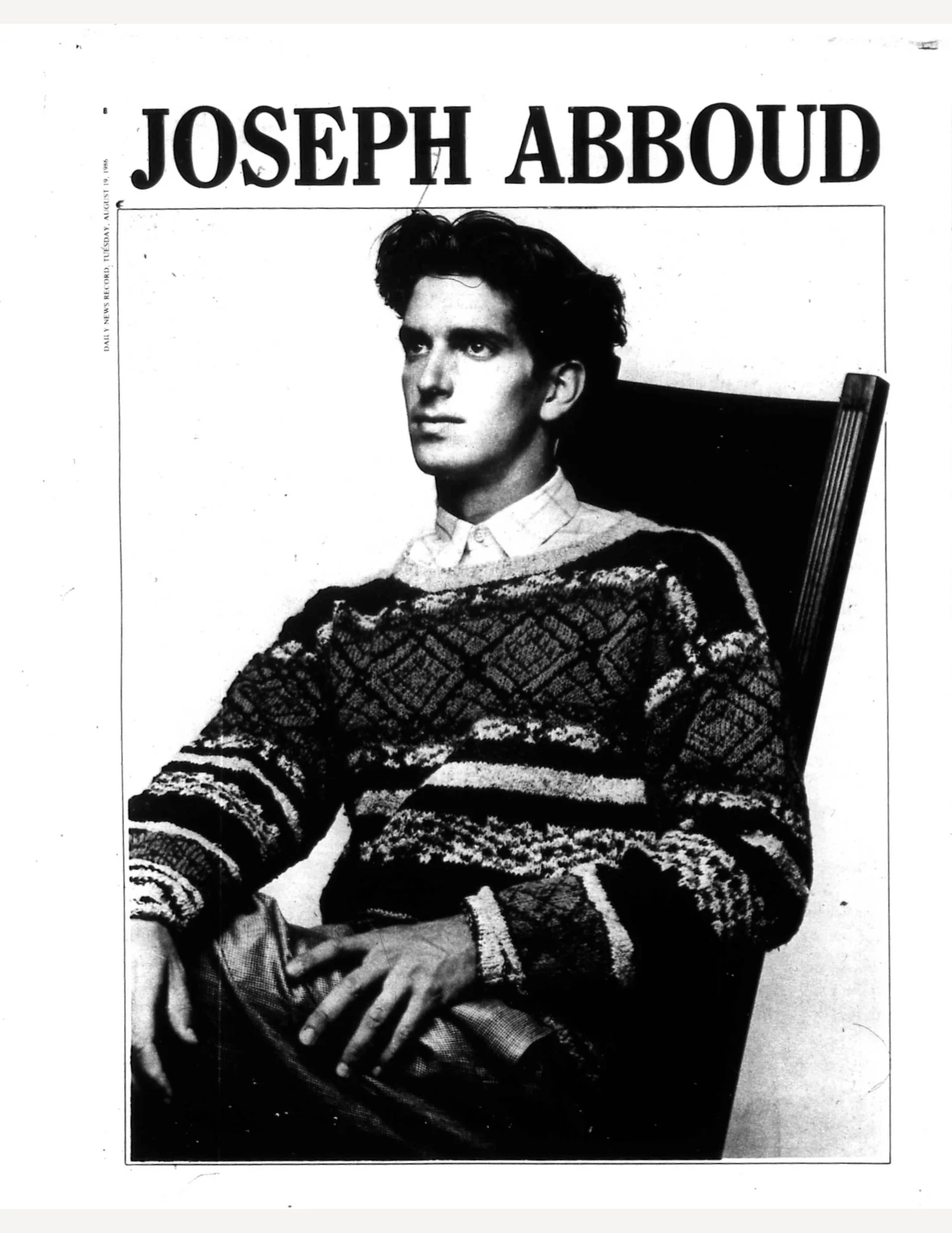 Joseph Abboud sitting in a chair with hands across his knee and thigh. He is wearing a patterned sweater and collared shirt.