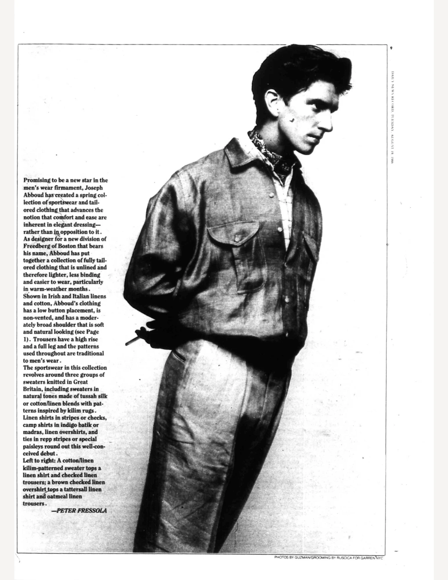 Joseph Abboud in a jacket and pants. He is leaning at a 45 degree angle with his hands behind his back, holding a cigarette.