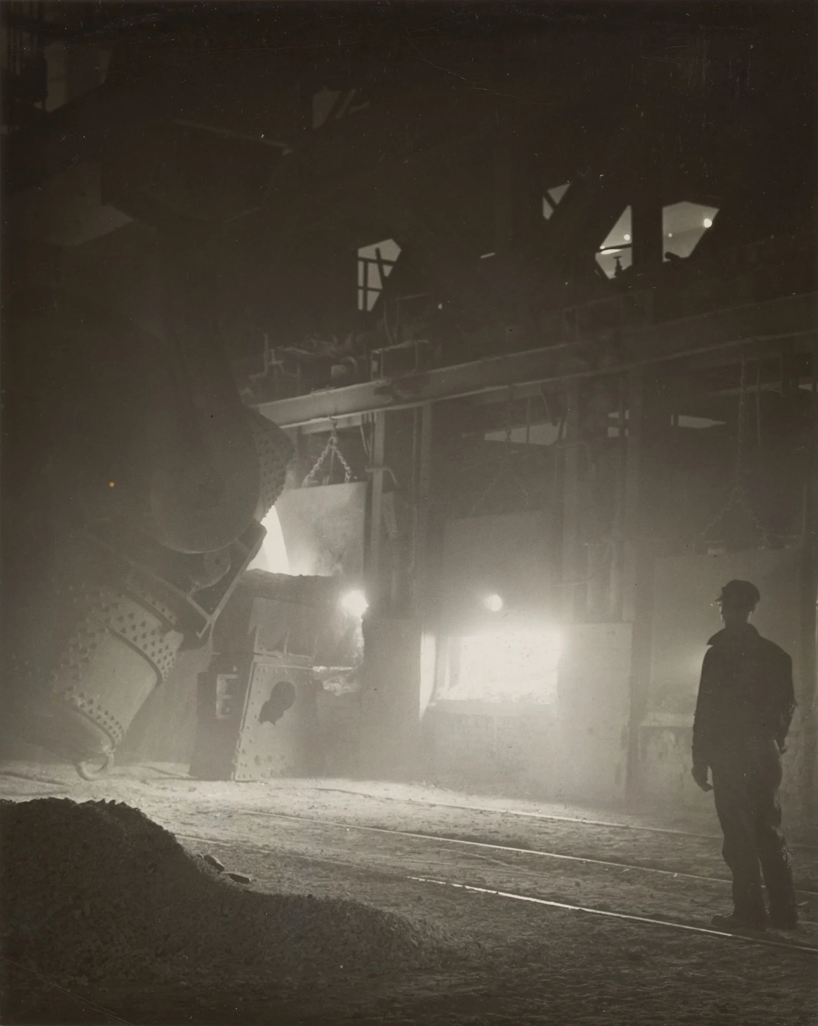 Silhouetted worker watches molten iron pour into open hearth furnace at Gary Steel Works.