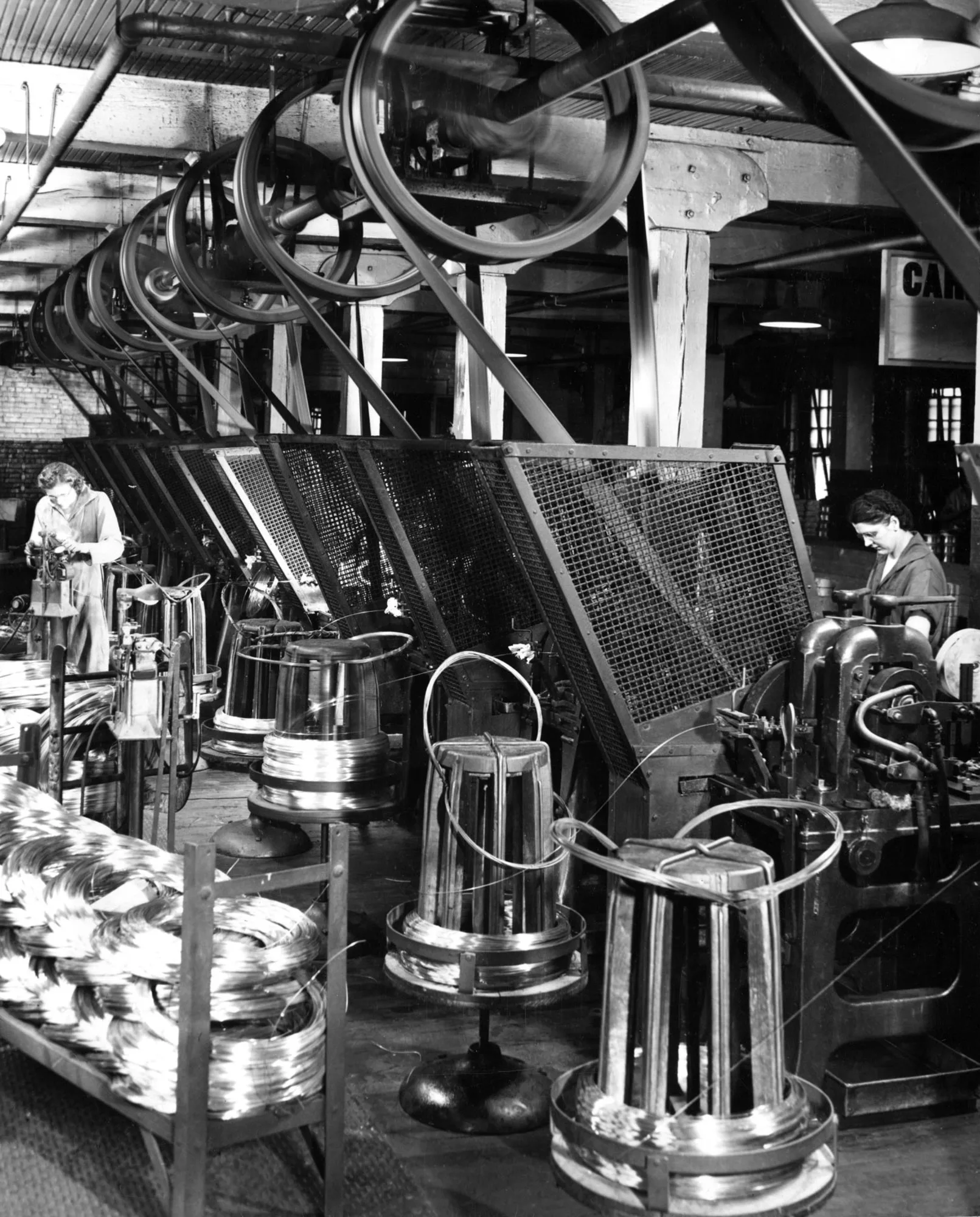 Workers operate belt-driven machines producing flat stitching wire with spools and coils throughout Newburgh Wire Works in Ohio.