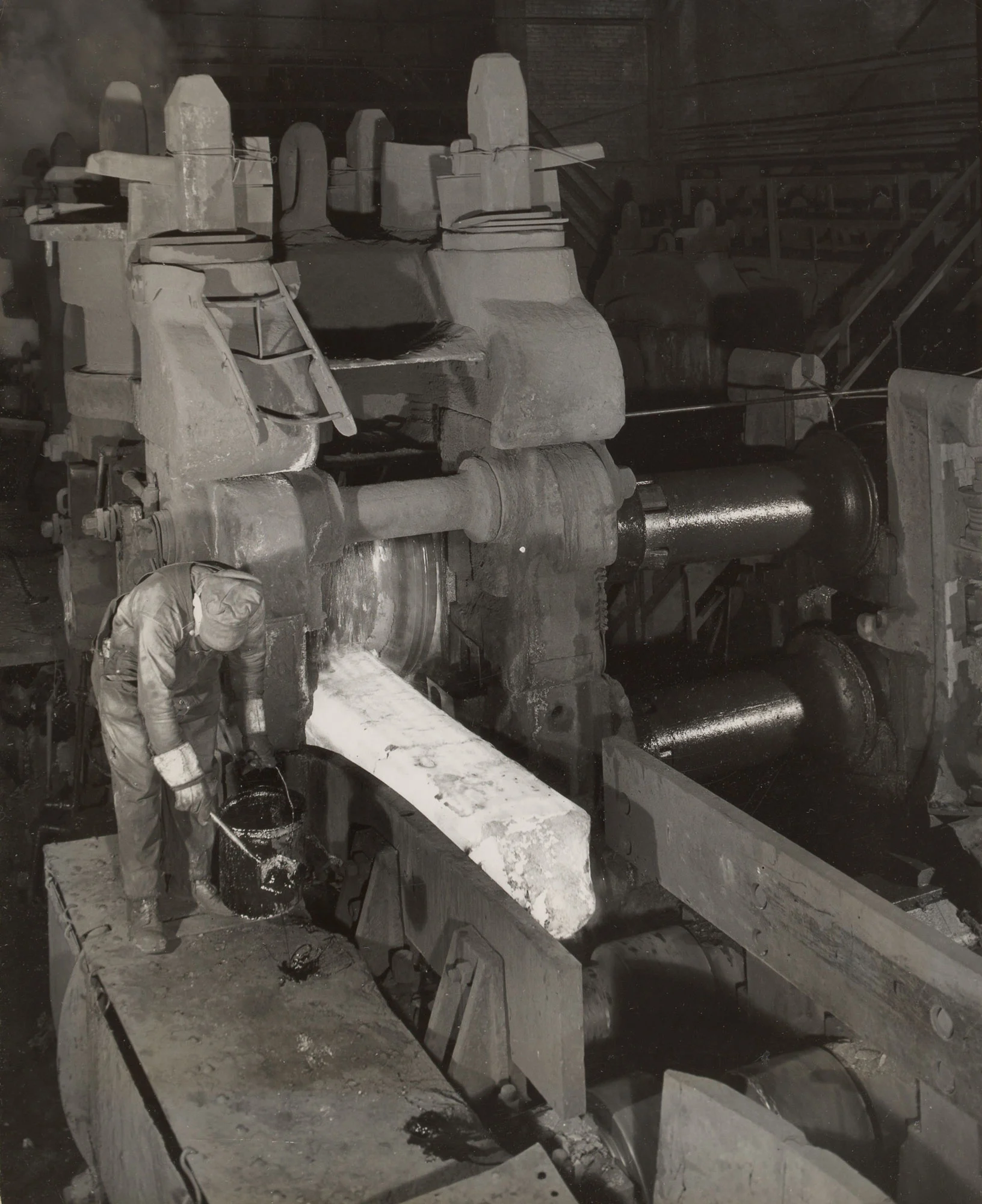 Worker oils table rolls as white-hot ingot exits second stand in 40-inch billet mill at Gary Steel Works.