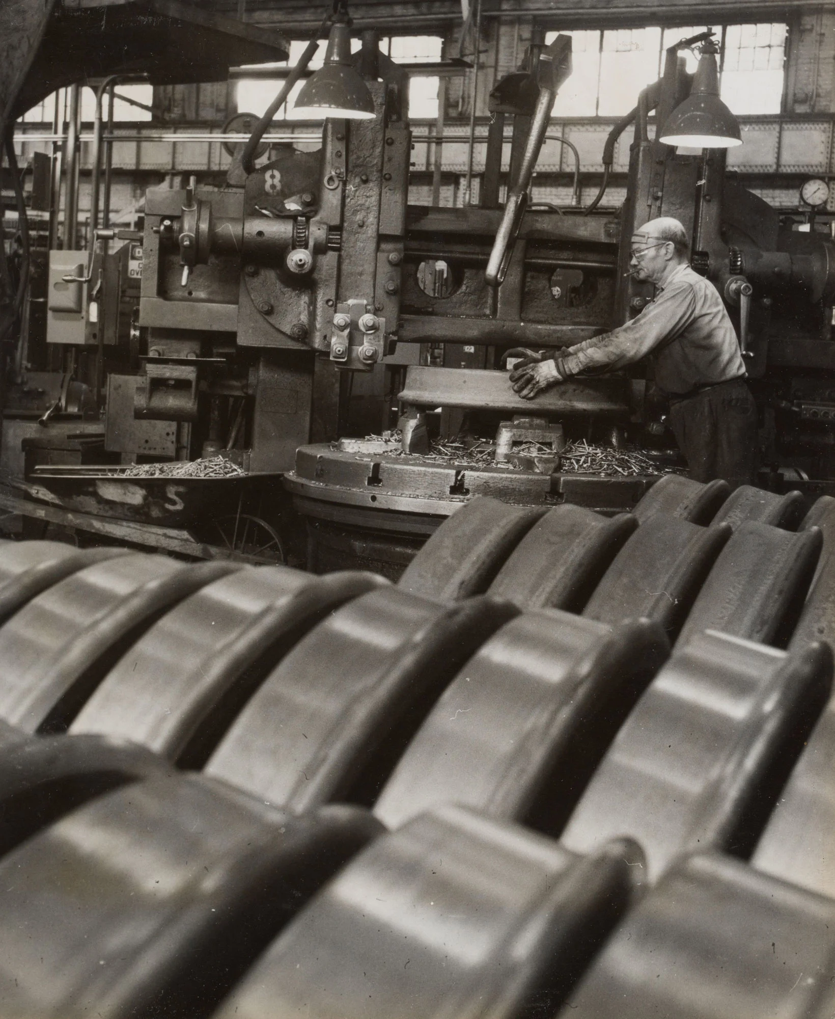 Operator machines tread of railroad car wheel as finished and unfinished wheels line foreground at Gary Steel Works.