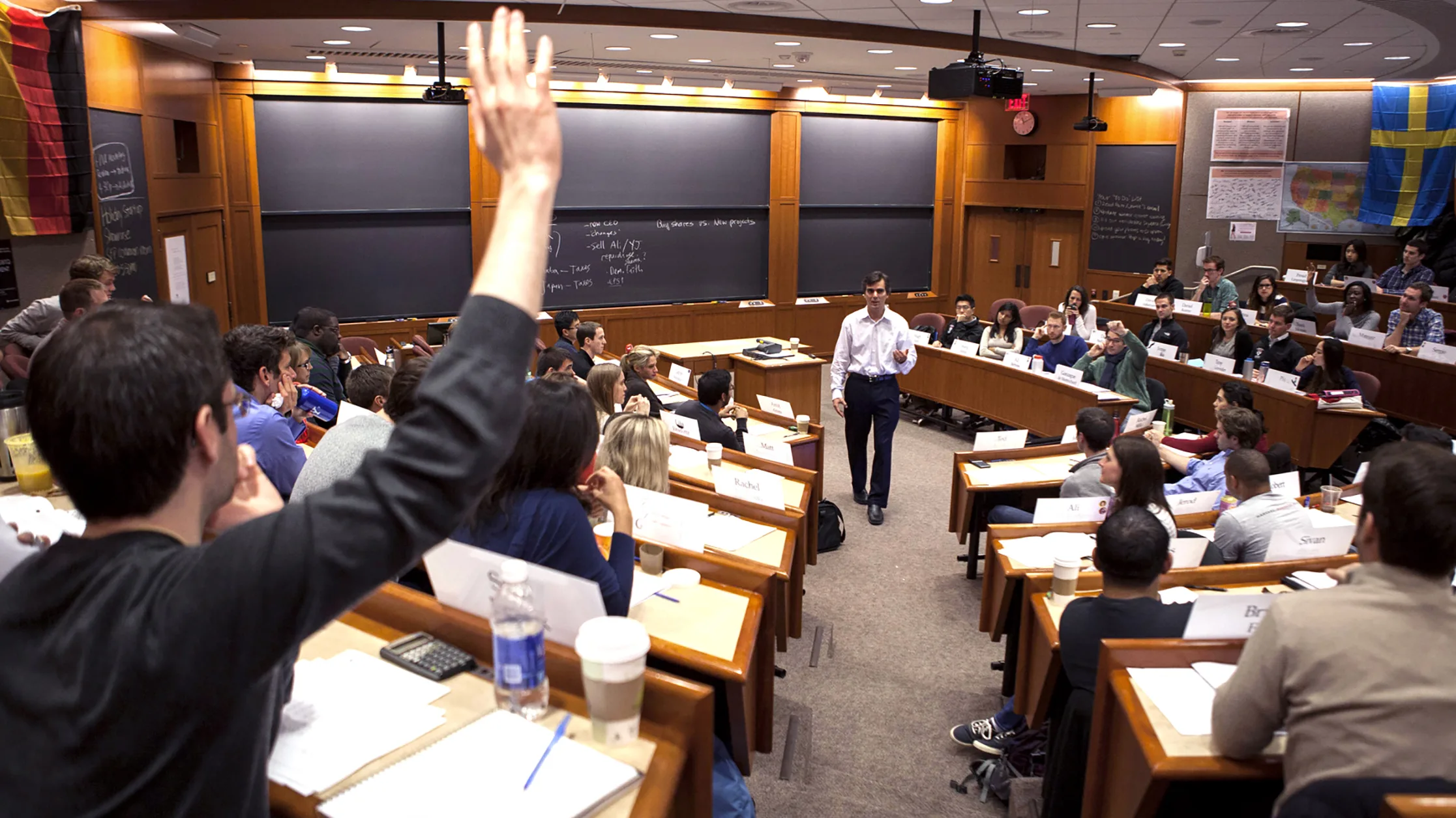 MBA students raising hands in classroom during a case discussion