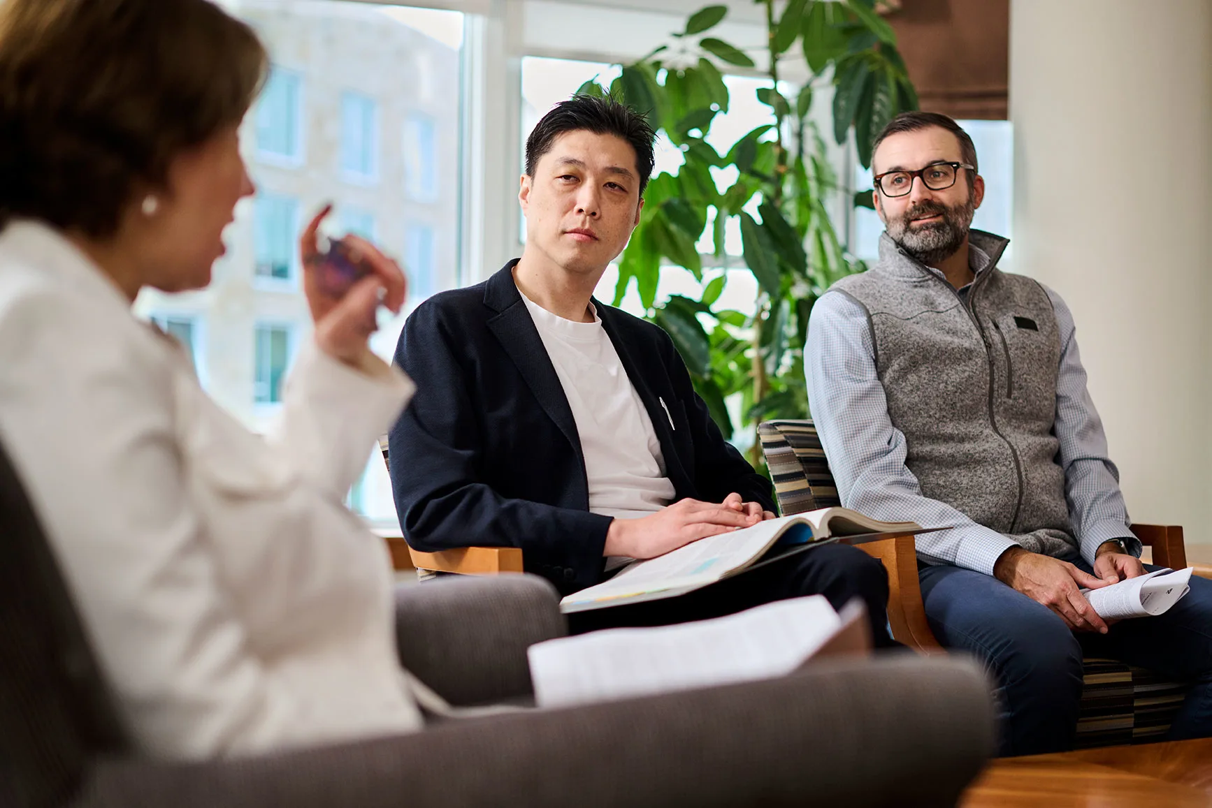 Two male participating executives listen as a female executive speaks and taking notes