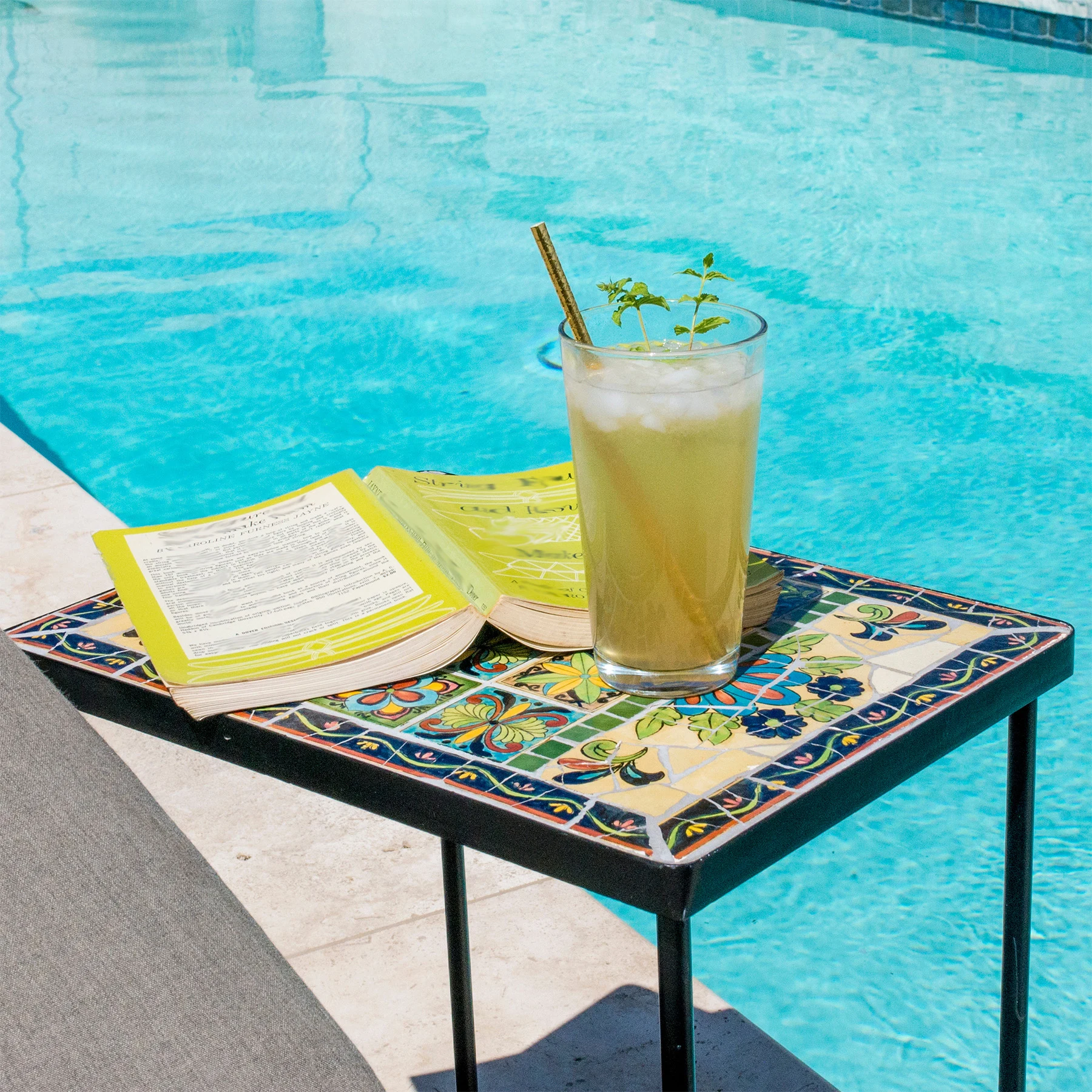 Poolside table with lemonade and an open, facedown yellow book upon it.