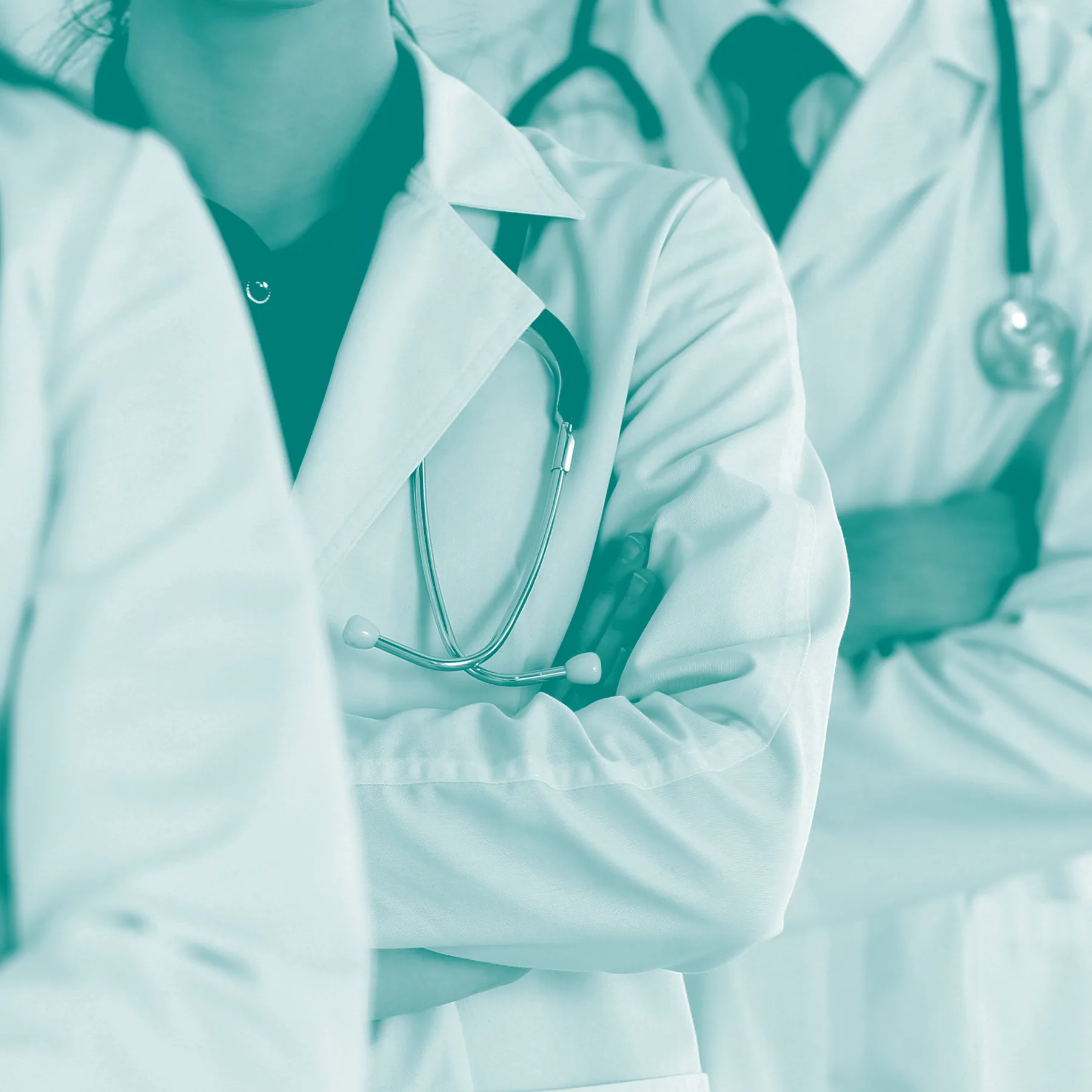 Close up on doctors wearing white coats and stethoscopes, standing with crossed arms.