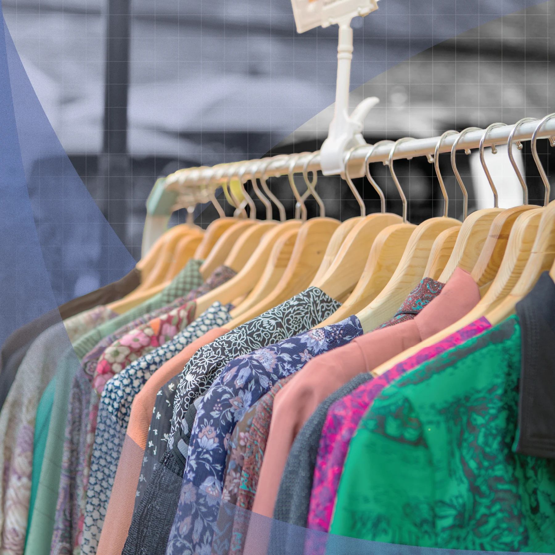 Patterned and solid-colored garments hanging on wooden hangers along a metal rack. The background is blurred, with a faint grid and translucent blue geometric overlays.
