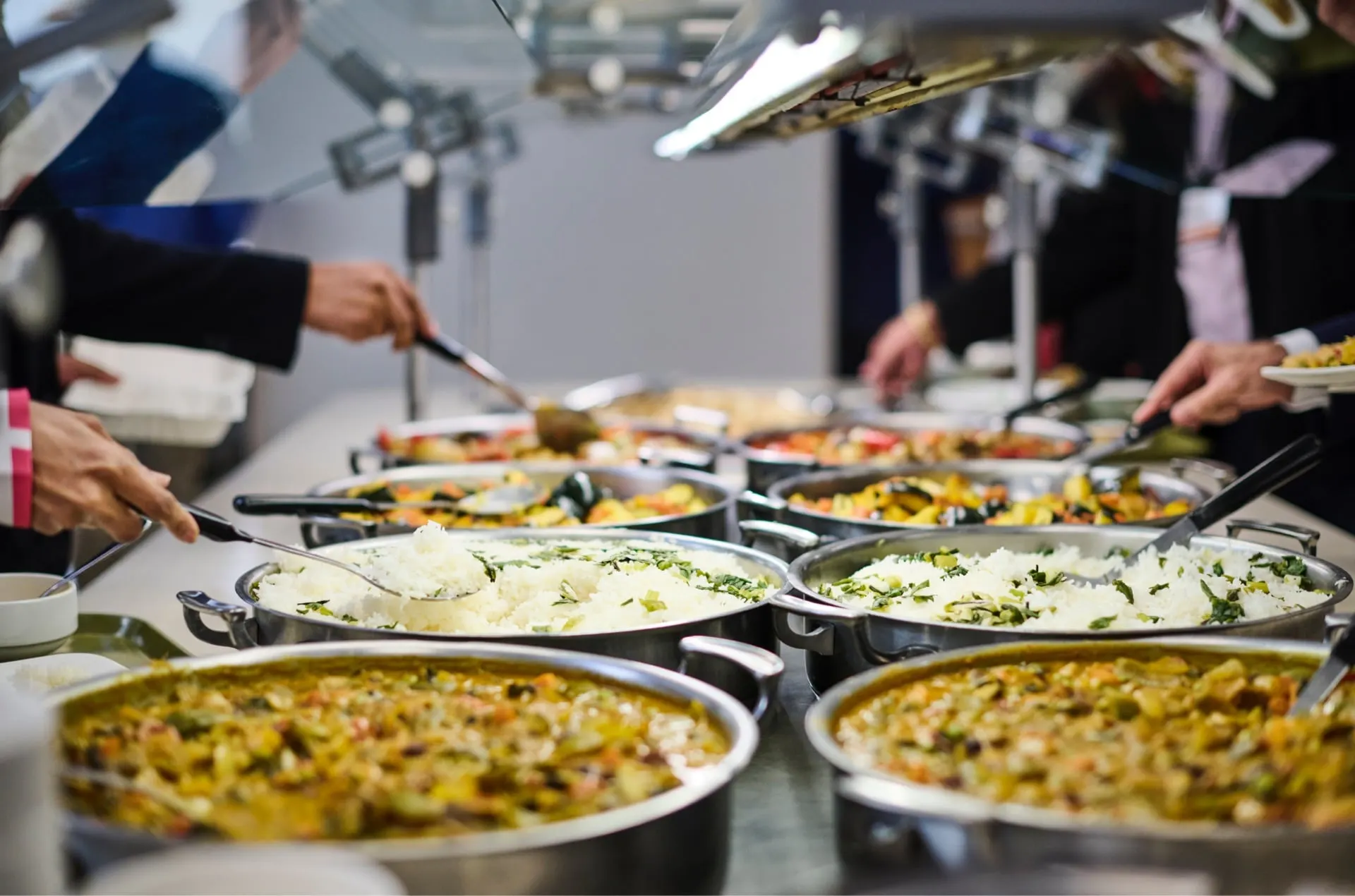 A buffet table filled with a variety of colorful dishes, including rice and vegetable curries, as people serve themselves food