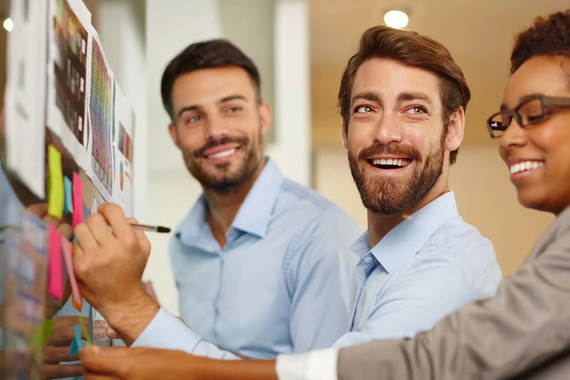 Smiling group for three executives collaborate, using colorful sticky notes on a glass board