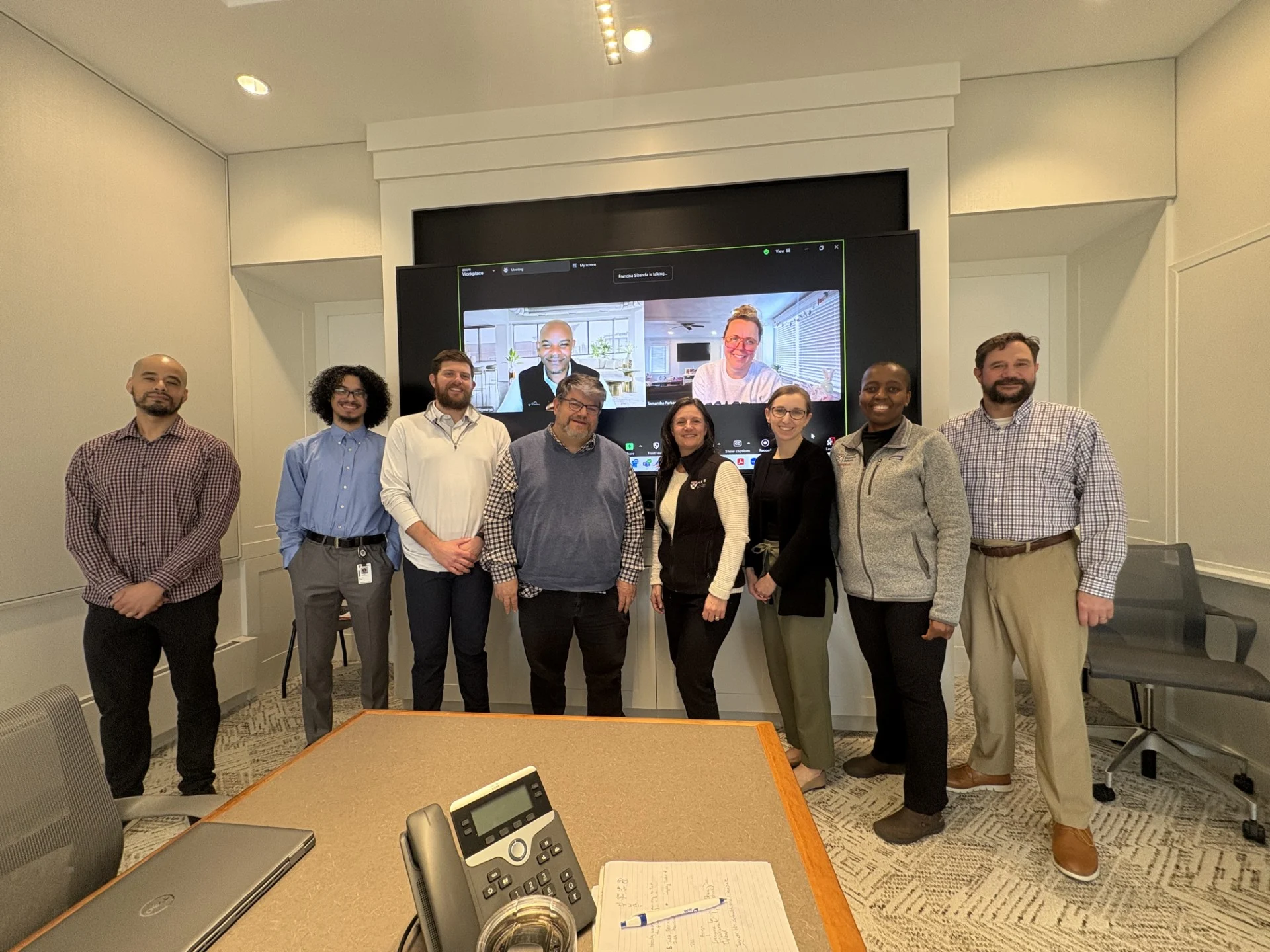 Most of the ITPSD team in person with two team members on the screen behind them via zoom.