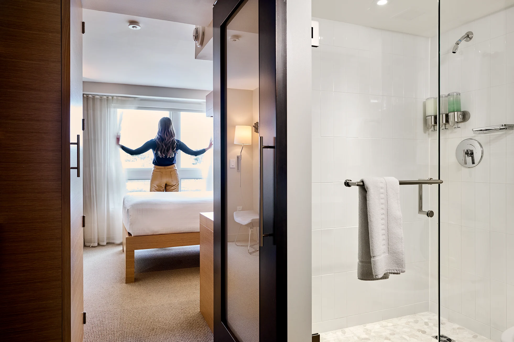 Residence hall bedroom and bathroom, with woman looking out a window