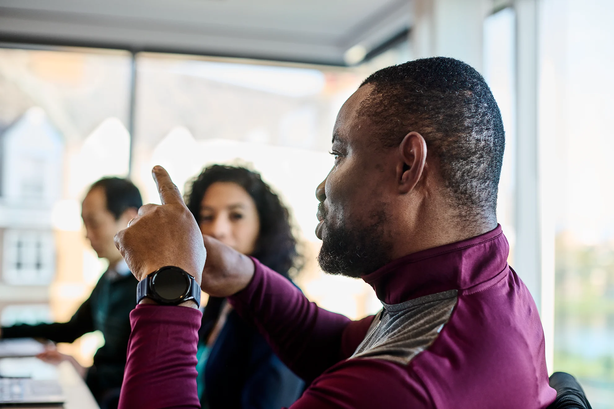 A male participant in red jacket talking and gesturing with his hands, while other other listening intently in the background