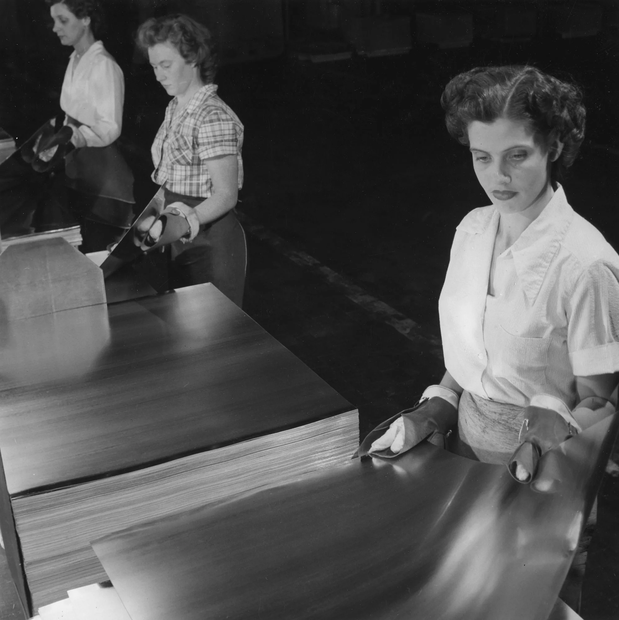 Three workers inspect and handle reflective tinplate sheets wearing gloves at Columbia Steel Company in Pittsburg, California.