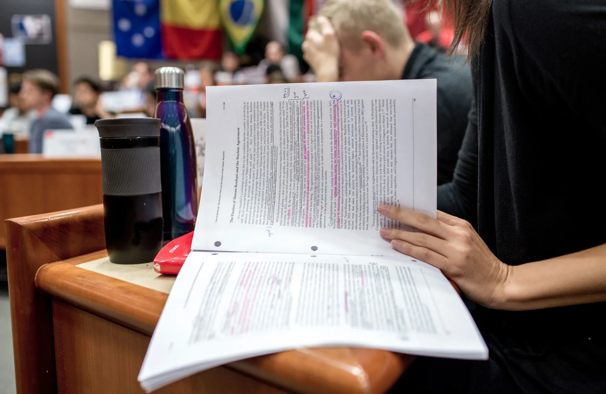 Close-up view of a highlighted and annotated paper on a desk in a classroom full of students.