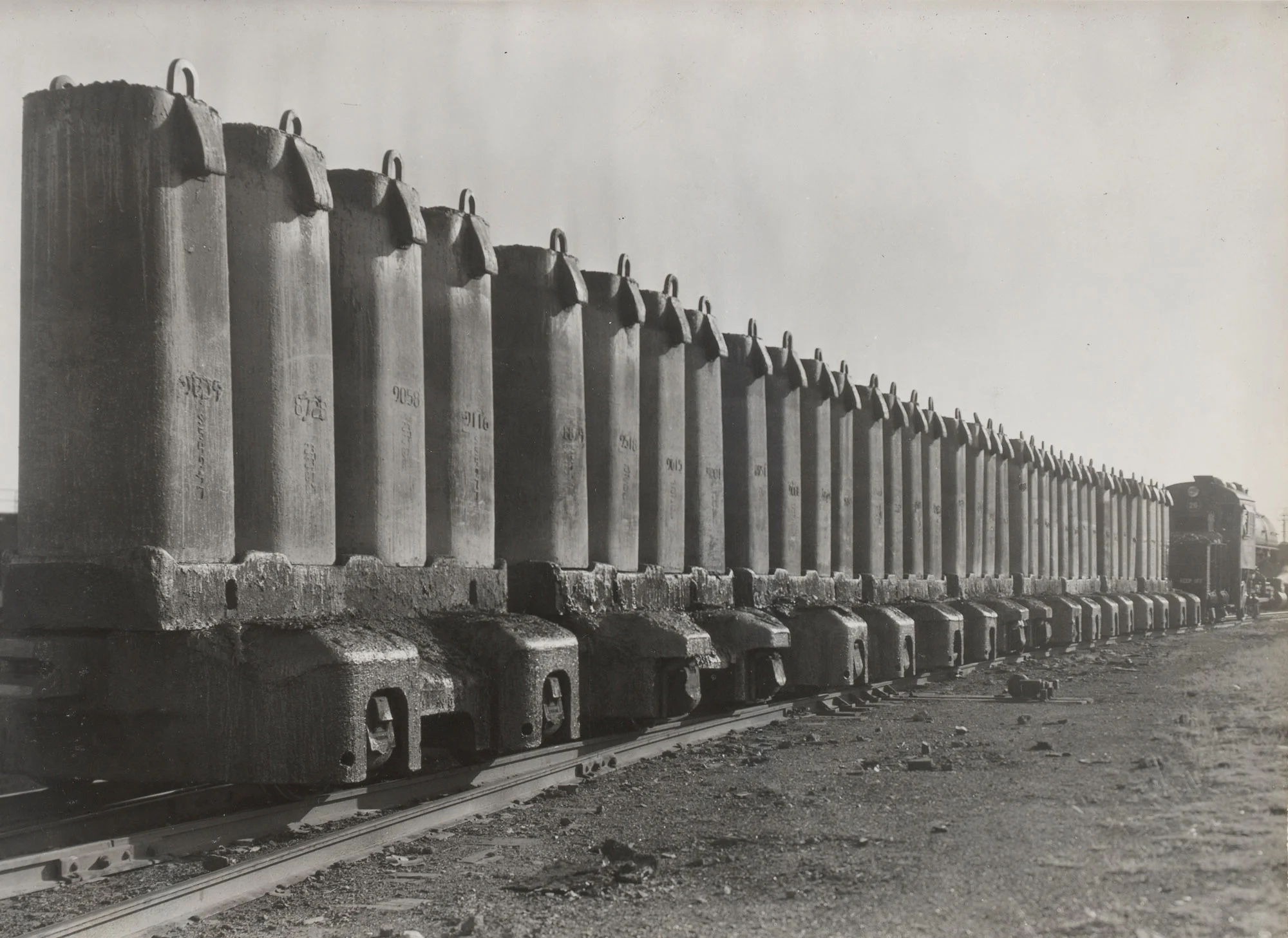 Long row of ingot molds on rail cars in transit at Gary Steel Works, with locomotive visible at far end.