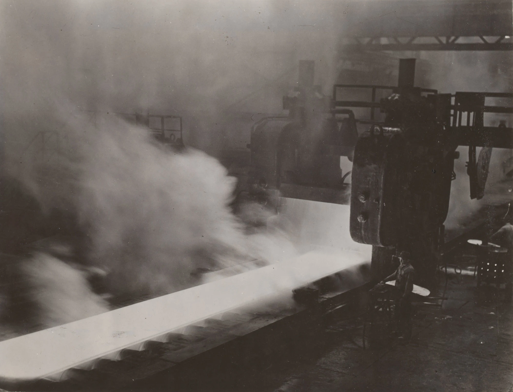 Steam rises as high-pressure water descales hot steel plate in mill at Gary Steel Works.