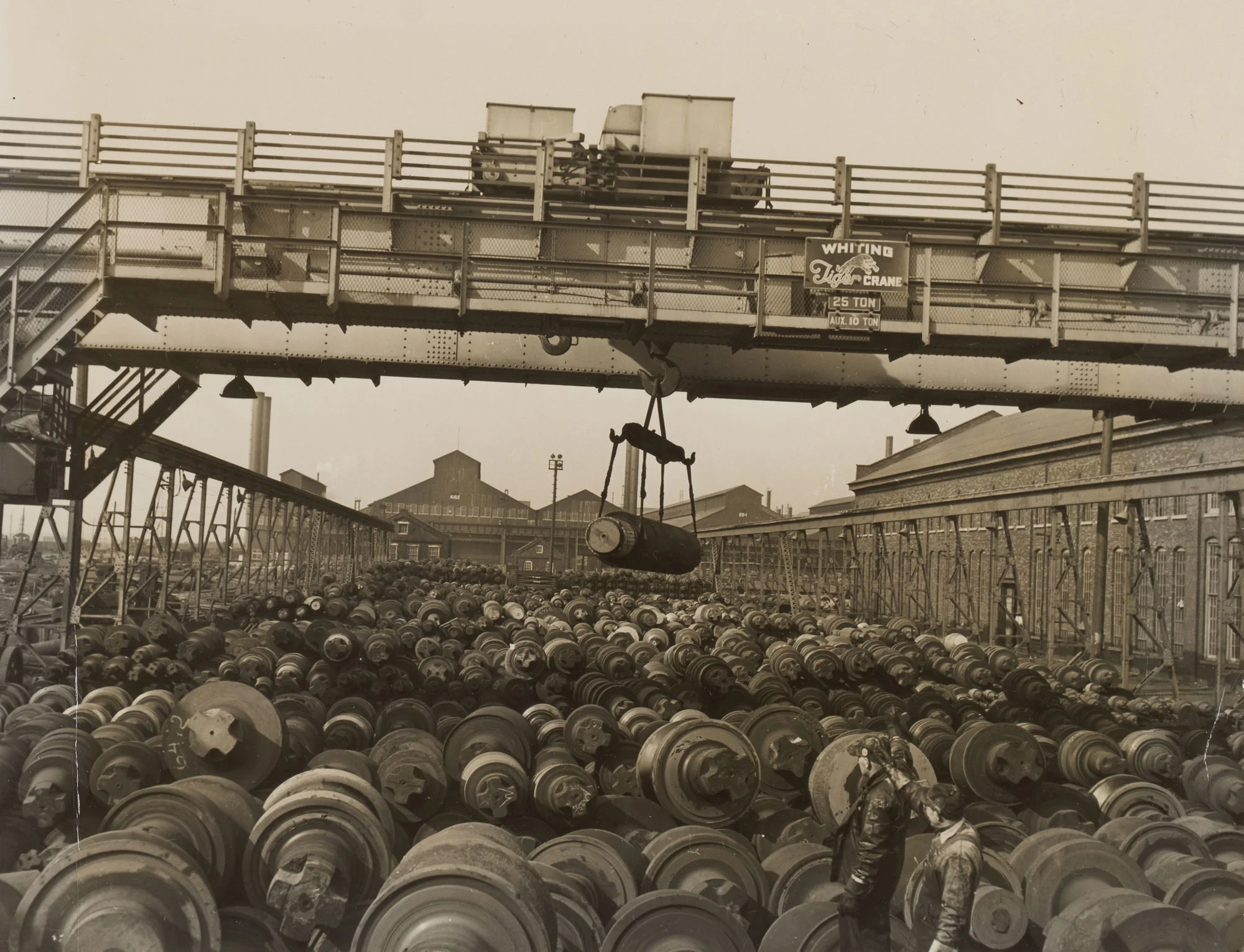 Overhead crane moves massive steel roll above densely packed roll storage yard at Gary Steel Works.