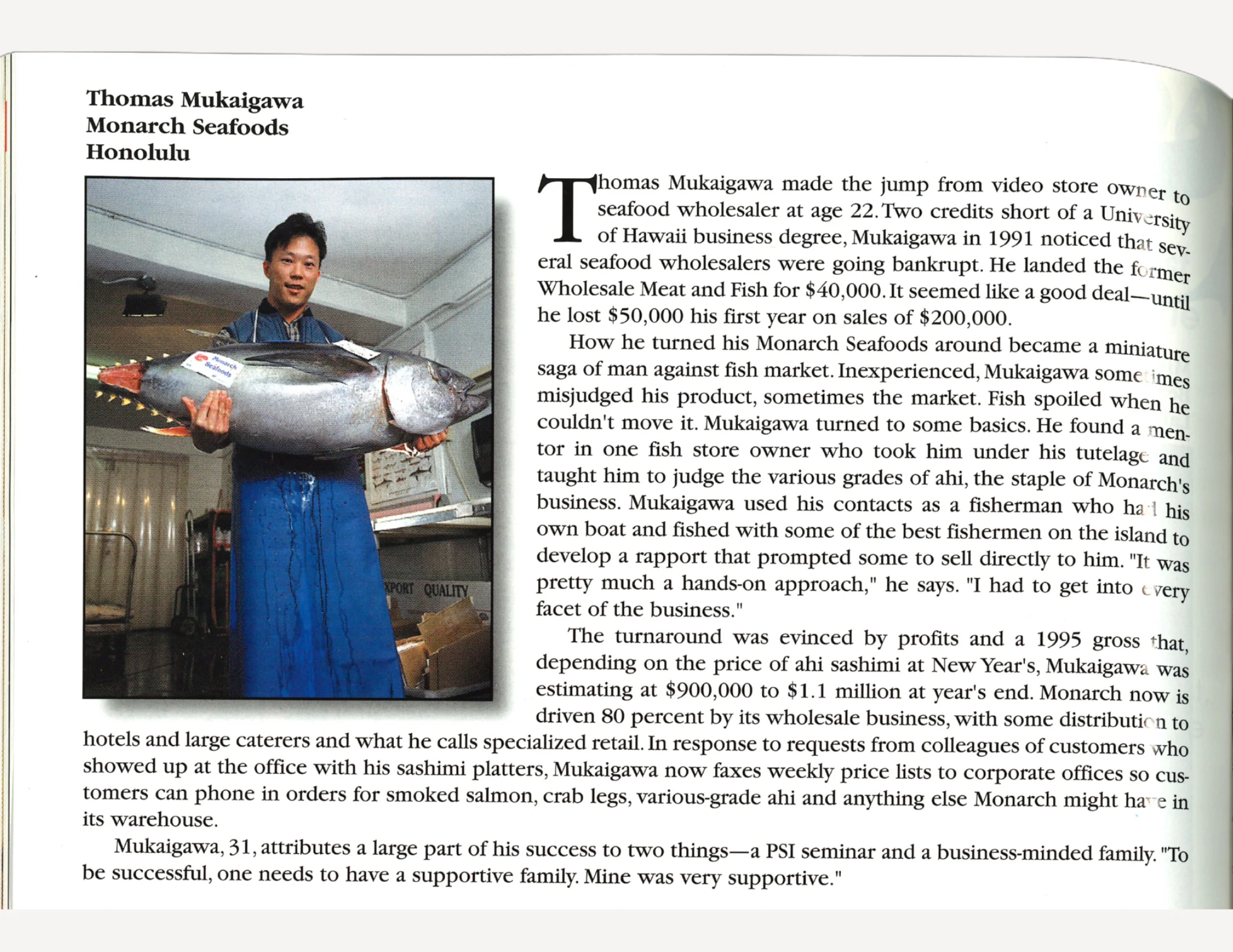 A man in a blue outfit holding a very large fish in both arms, next to text