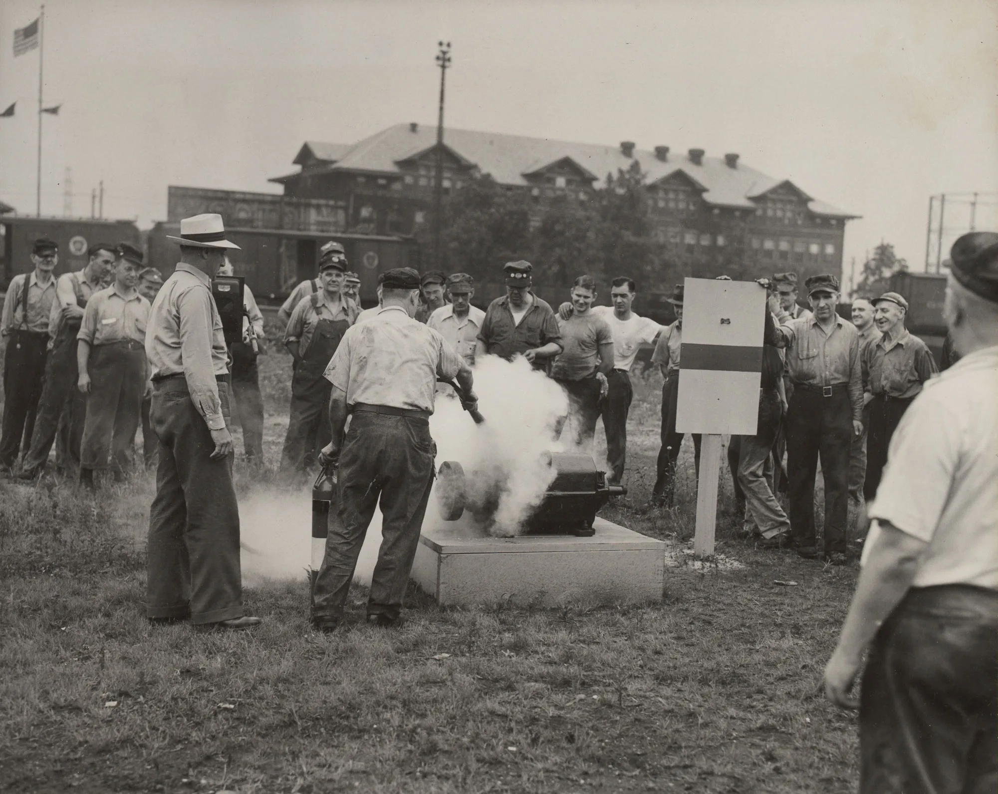 Worker demonstrates CO2 extinguisher use on simulated motor fire as group observes at Gary Steel Works.