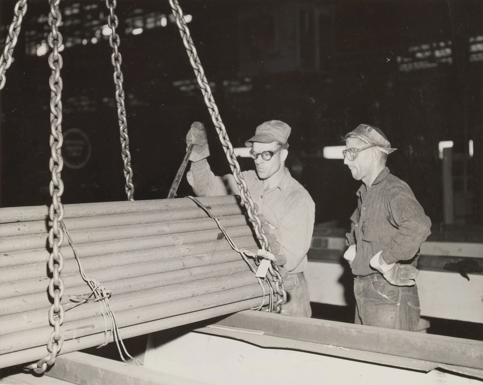 Experienced worker instructs new employee on safely cutting wire from bundled steel rods at Gary Steel Works.