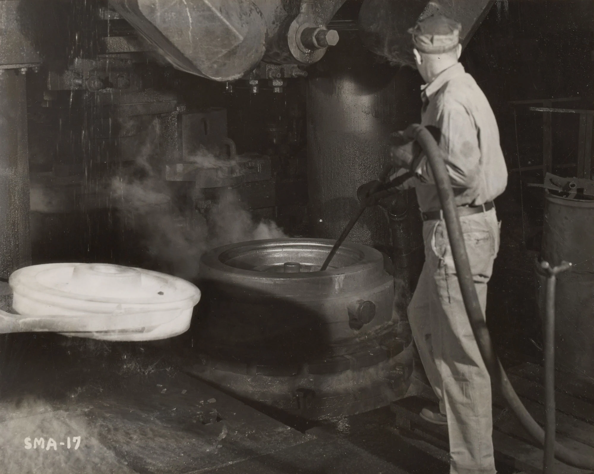 Worker uses compressed air to clean die after shaping red-hot 28-inch freight car wheel at Gary Steel Works.