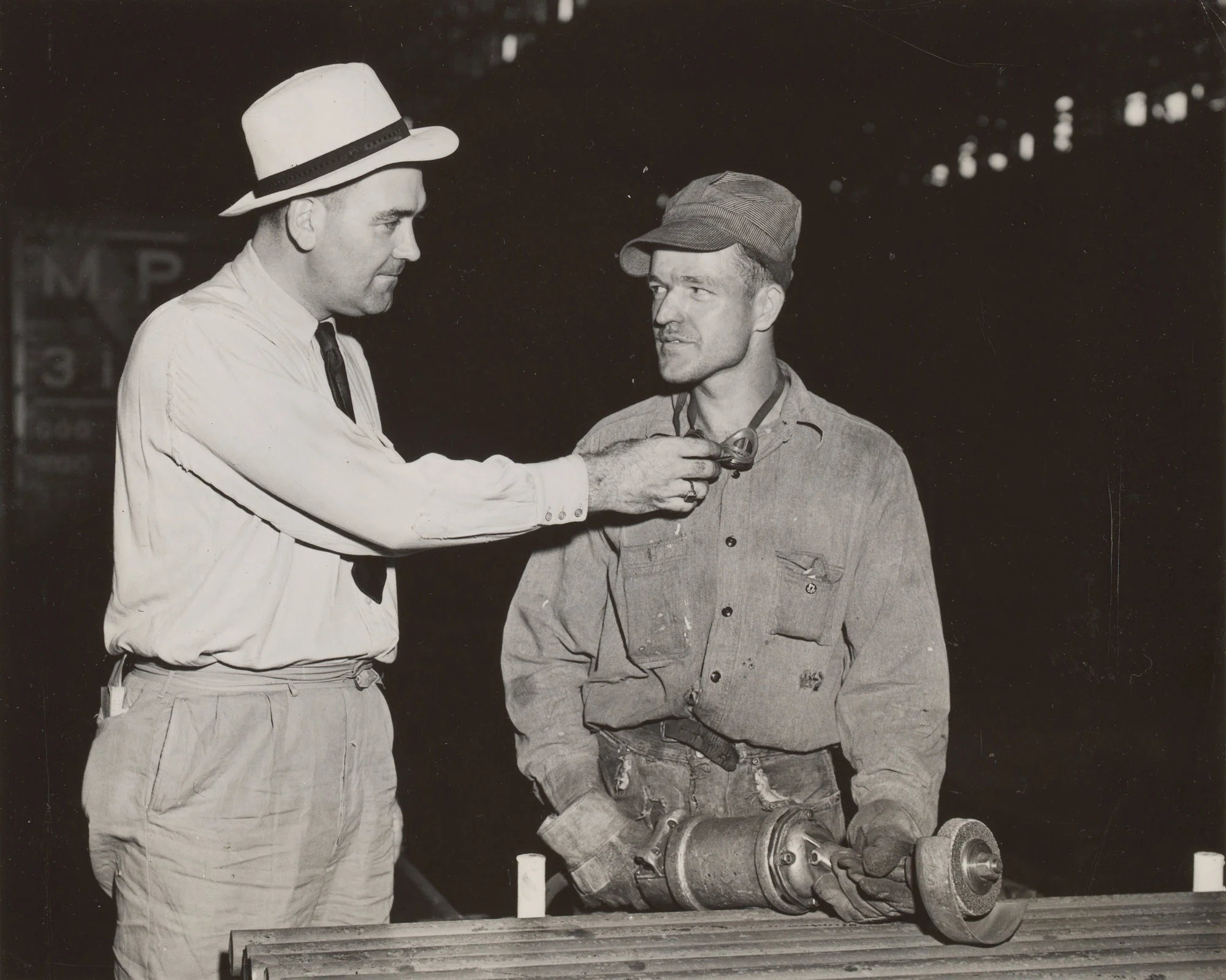 Supervisor instructs new worker on grinder safety while demonstrating proper use of goggles at Gary Steel Works.