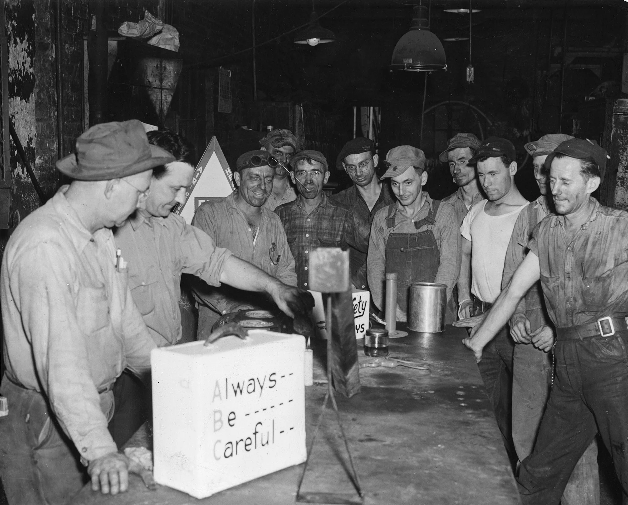 Group of steelworkers watch a safety demo on gasoline fumes with a sign reading "Always Be Careful" at Gary Works, Indiana.