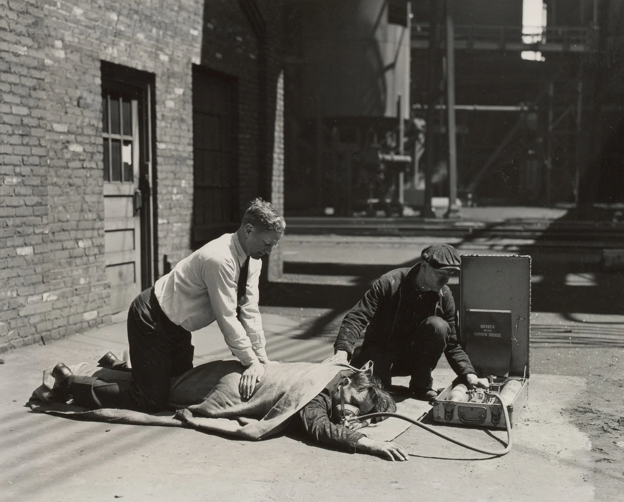 Two workers practice resuscitation with oxygen inhalator and prone pressure method outside at Gary Steel Works.