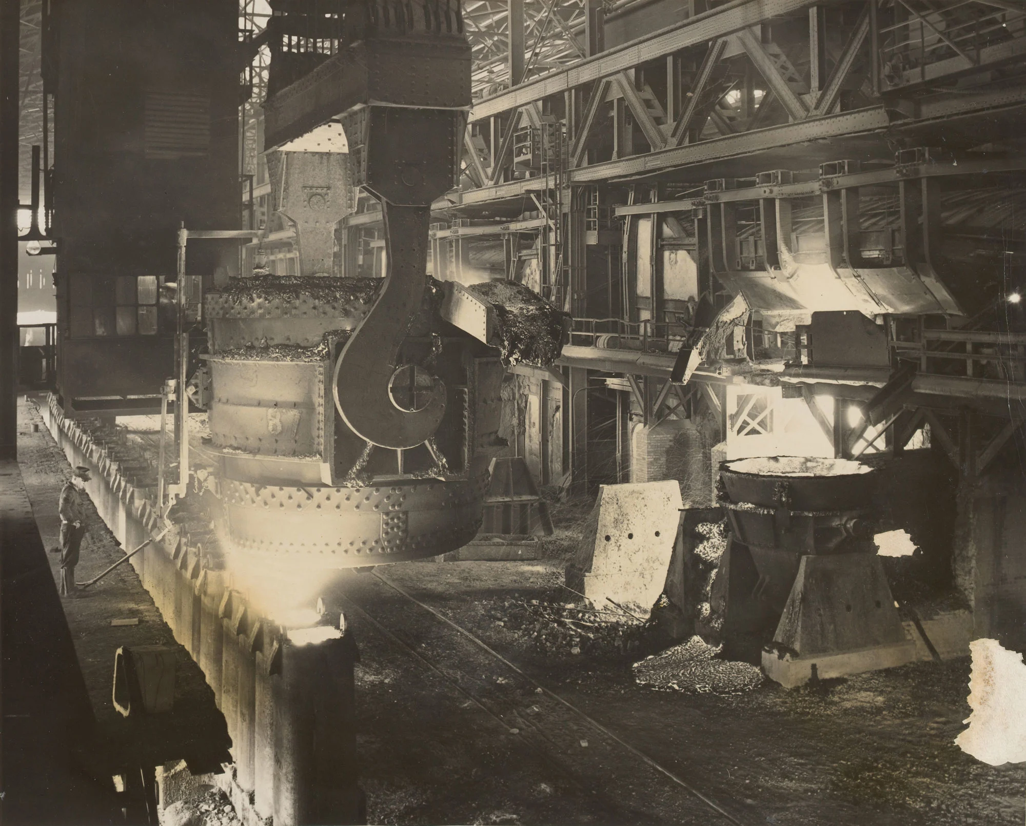 Steel pourer monitors molten stream filling ingot mold as crane operator positions ladle at Gary Steel Works.