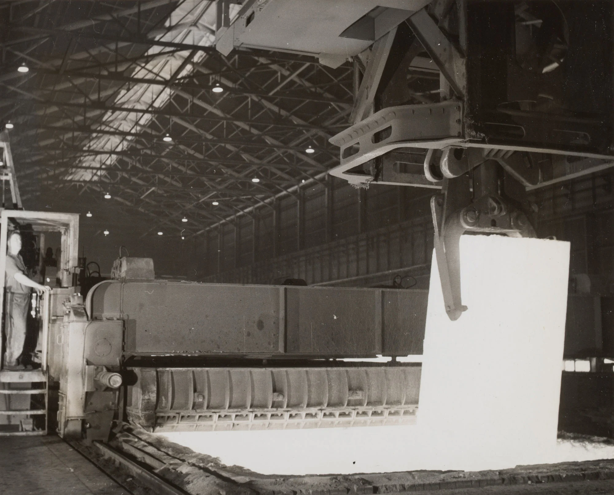 Glowing ingot lifted from soaking pit at 45-inch slabbing mill in Homestead Works as worker observes.