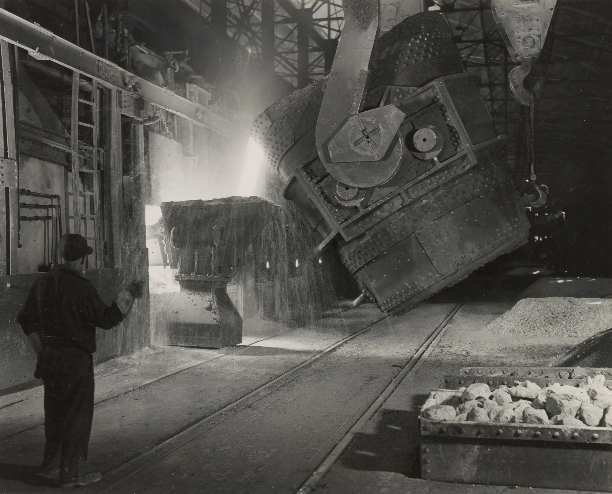 Large ladle pours molten iron into open hearth furnace as a worker oversees the process at Gary Steel Works.