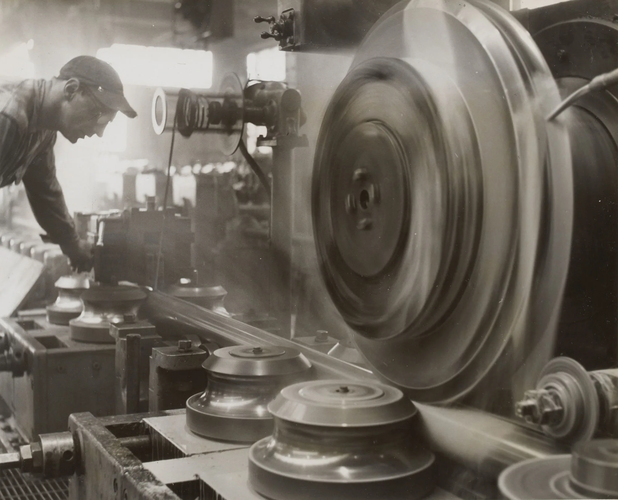 Person operating large industrial machinery with spinning metal rollers in a factory setting.