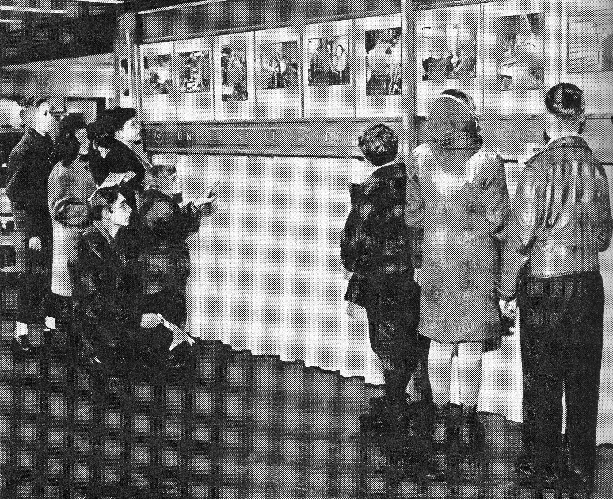 Group of adults and children view U.S. Steel’s “Steel at War” photo exhibit displaying wartime production scenes in 1944.