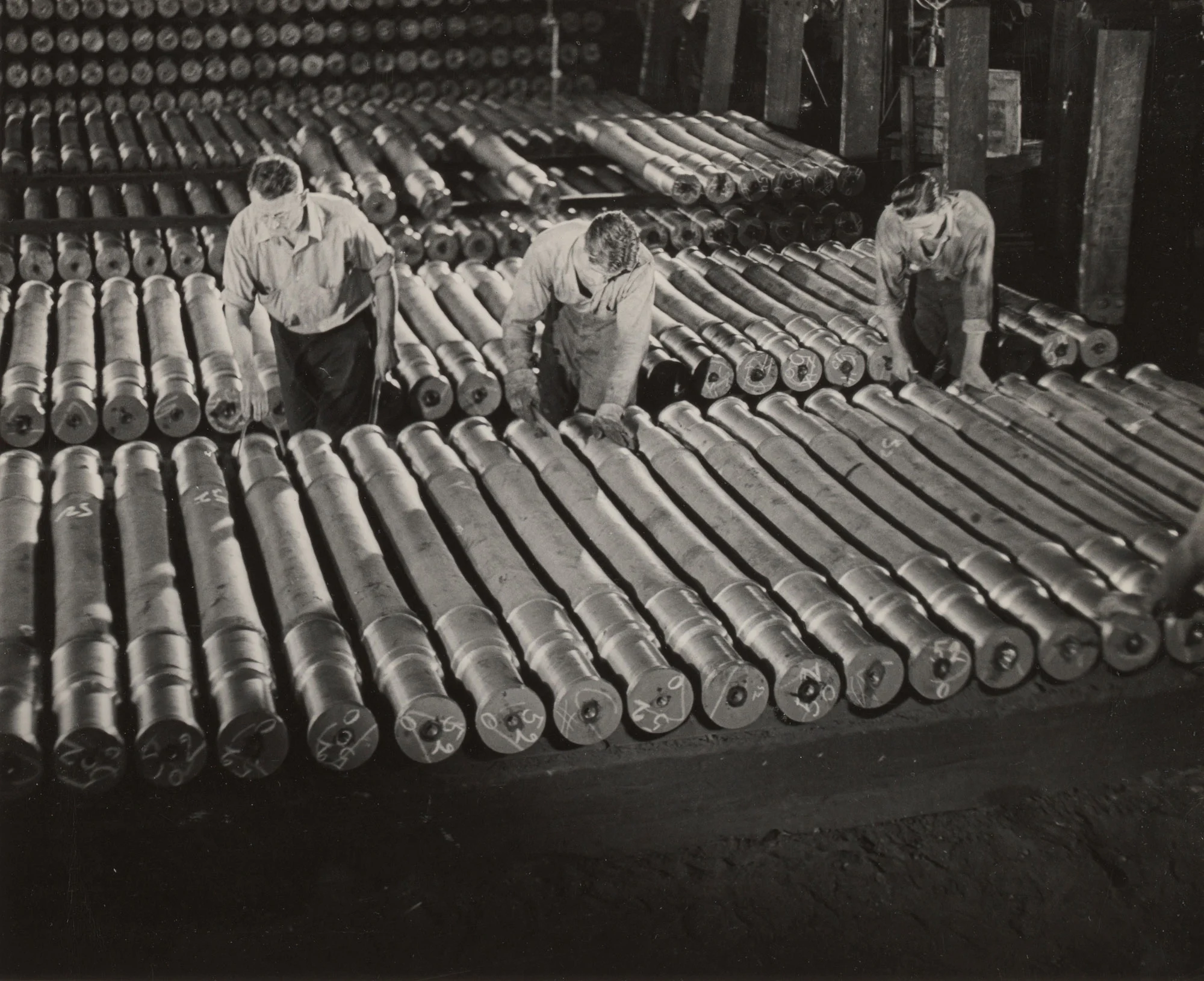 Three workers inspect rows of finished railroad axles at Gary Steel Works.