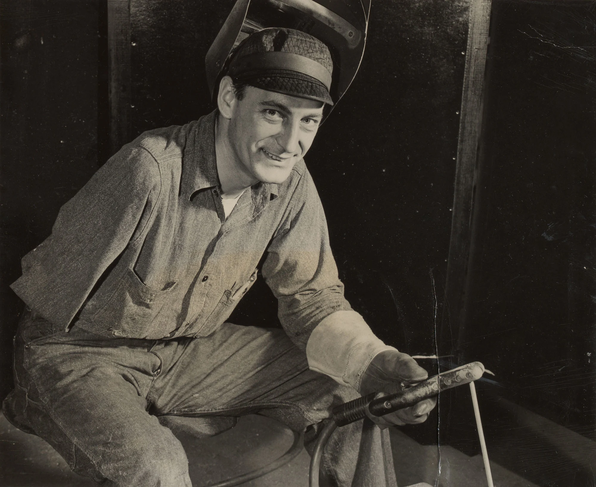 Smiling welder with one arm holds torch while seated in welding shop at Gary Steel Works.