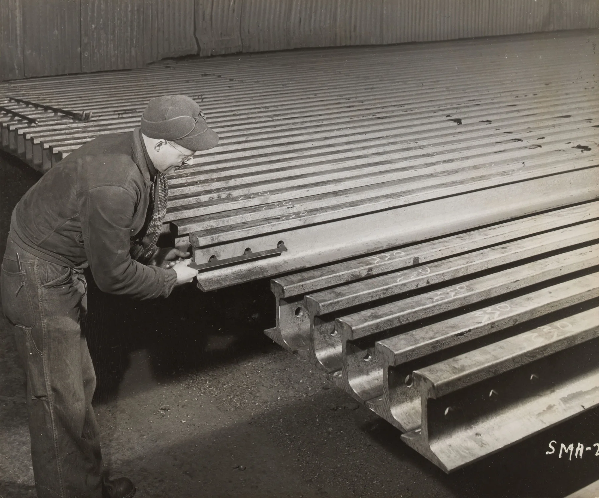 Inspector gauges bolt hole placement on new steel rail sections at Gary Steel Works rail mill.