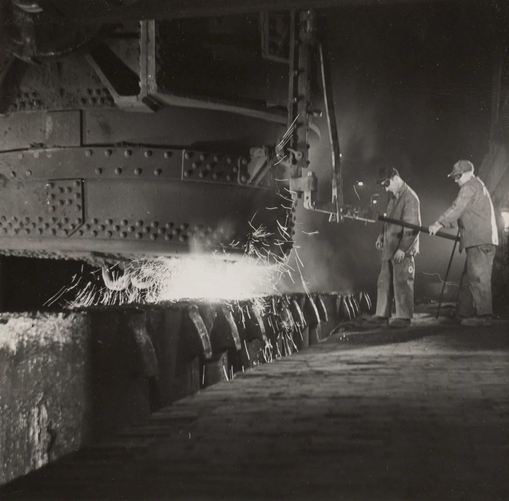 Two workers teem molten steel from ladle into ingot molds at Gary Steel Works open hearth shop.