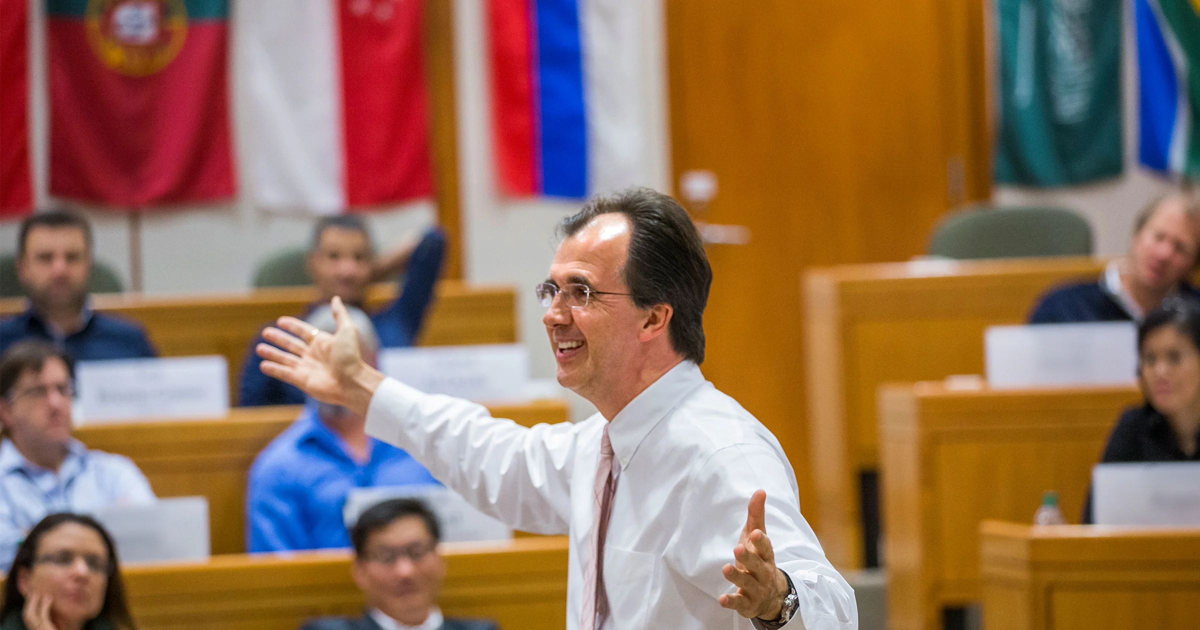 Faculty member teaching executive education participants in HBS classroom adorned with international flags